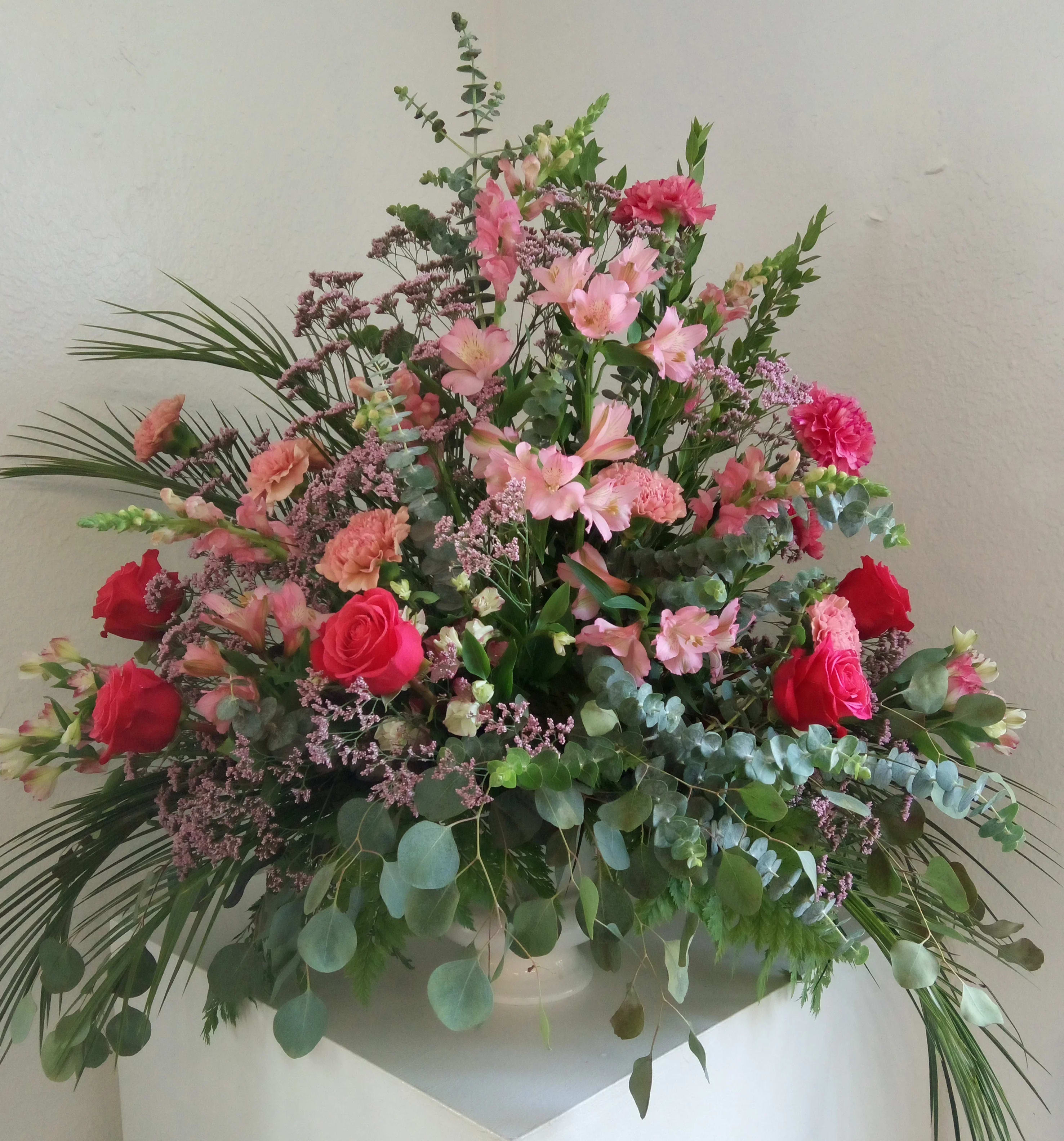 Large pink and red floral arrangement in a white vase
