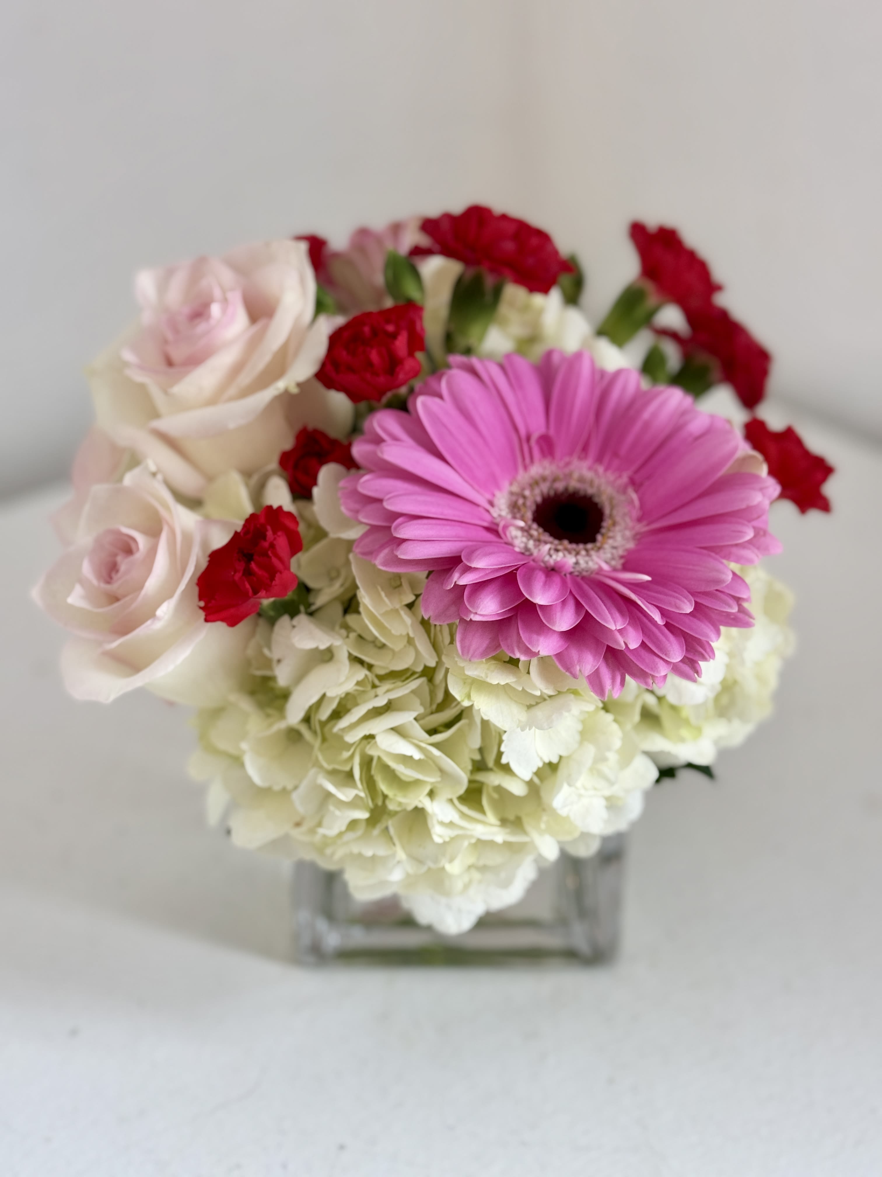 Pink gerbera daisy and roses in a square glass vase