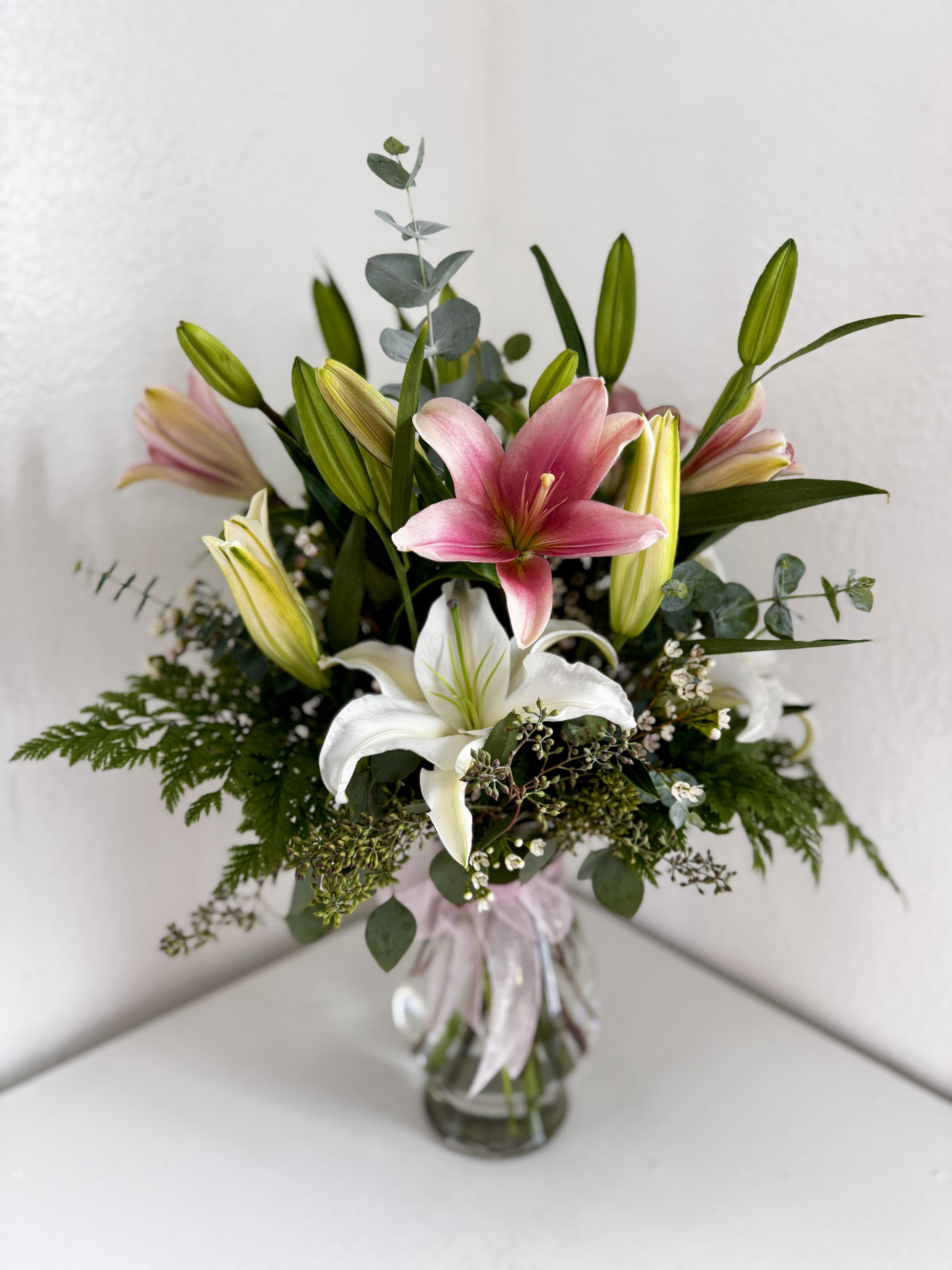 Pink and white lilies in a glass vase with greenery