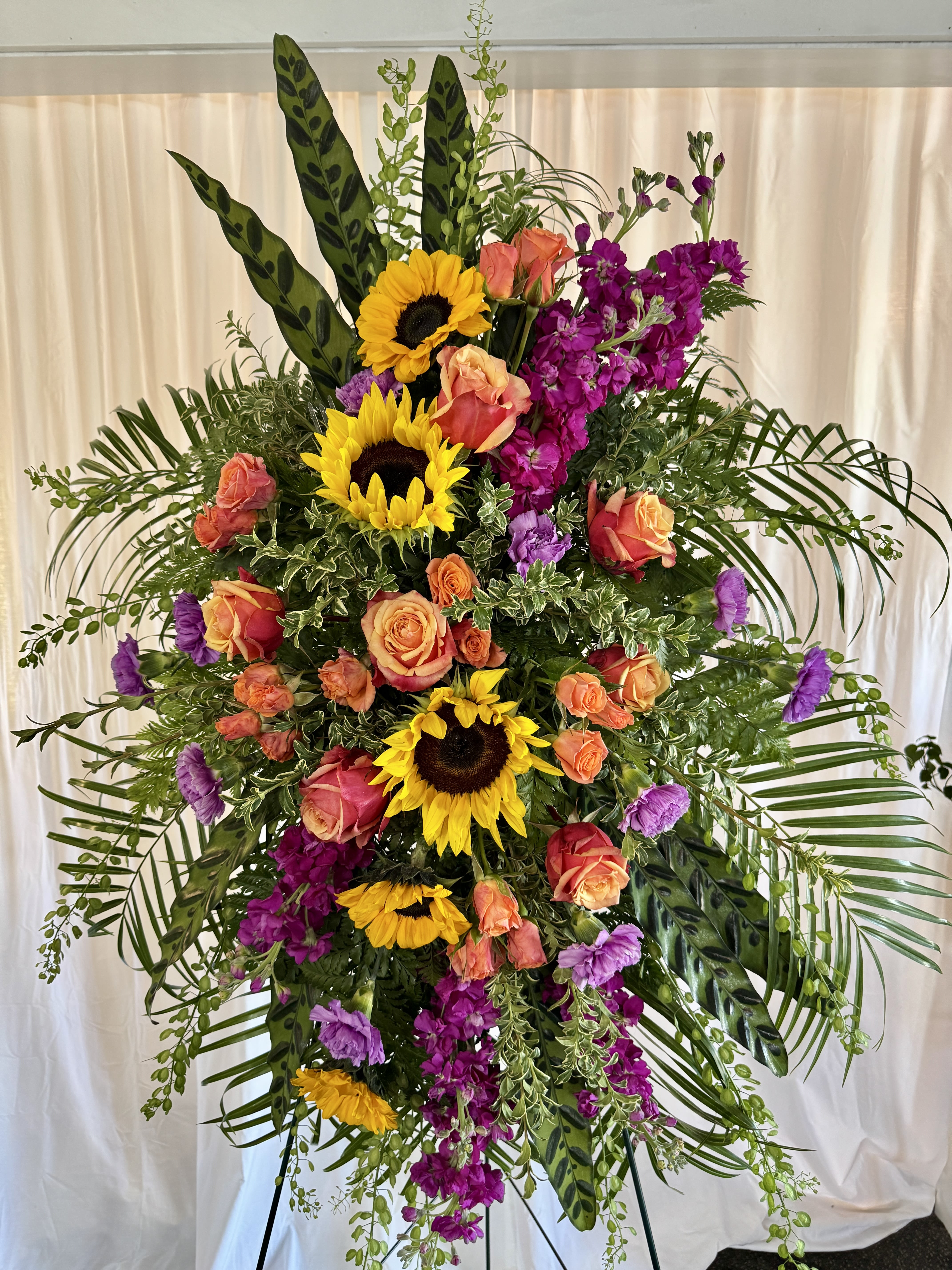 Tall standing floral spray with sunflowers, roses, and purple blooms