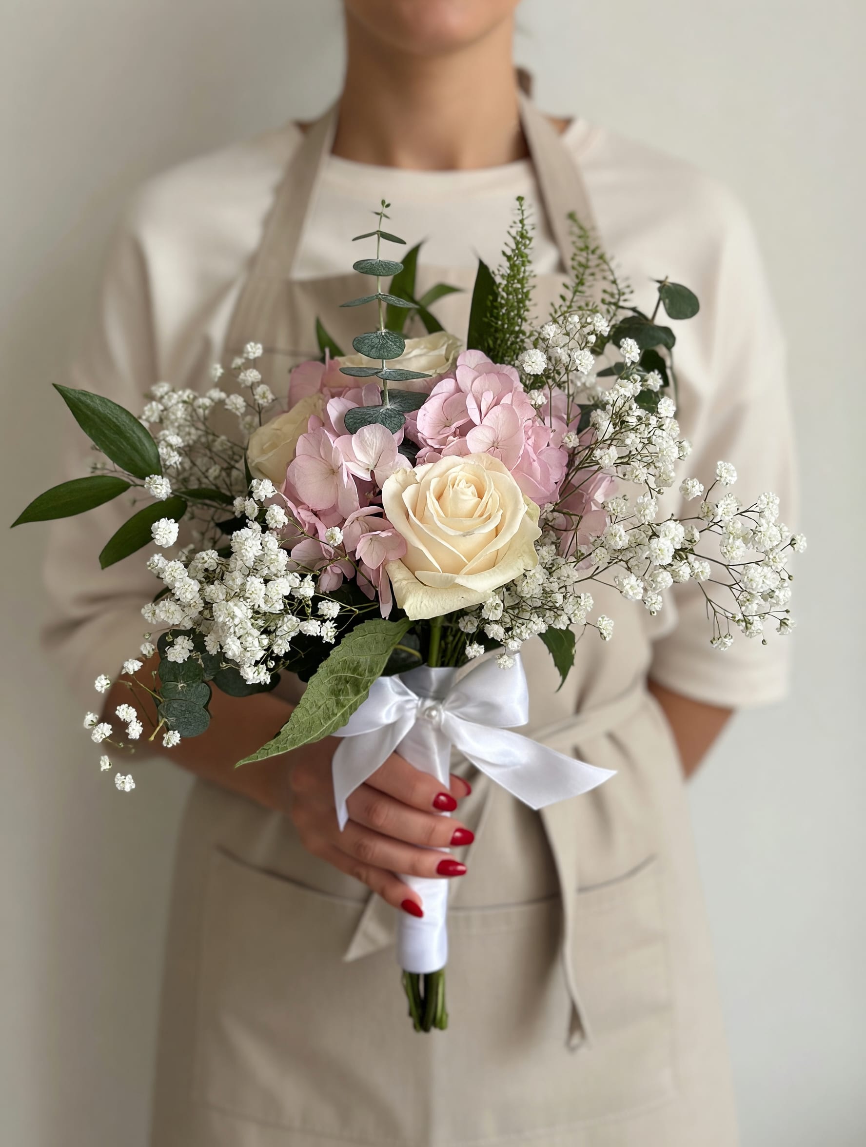 Mini Prom Bouquet Pink &amp; White - Cream roses paired with soft pink hydrangeas and airy sprays of baby's breath create a delicate, romantic prom bouquet that's equally at home for anniversaries, birthdays, or a heartfelt thank-you. This mini prom bouquet in pink and white reads as fresh and airy-the soft rose petals and cloud-like hydrangea blooms will make the person you're thinking of feel gently celebrated without overwhelming them.  Hand-tied for a full, rounded silhouette, the arrangement is finished with eucalyptus-like green foliage for subtle contrast and a white satin ribbon wrap around the handle for a polished, gift-ready look. The wrapped bouquet handle makes it easy to carry or present, and the compact size is perfect for a pocket corsage alternative or a tight formal look.  Give this bouquet to someone who appreciates classic, understated romance-she'll feel seen and cherished whether it's a graduation, a small celebration, or just because. For best results, keep stems in fresh water and out of direct heat; the combination of roses, hydrangeas, and baby's breath favors cool, well-hydrated care.