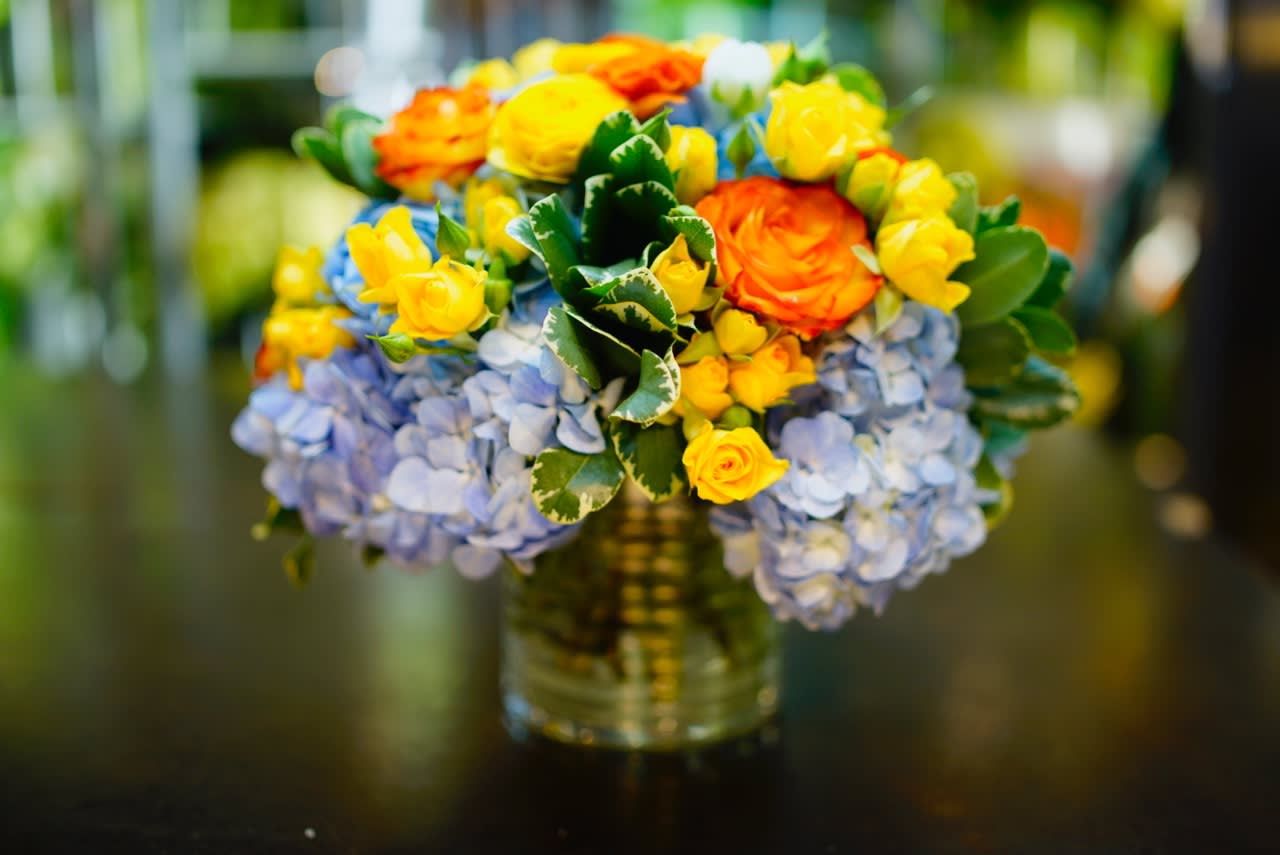 Bouquet of orange and yellow roses with blue hydrangeas in a glass vase