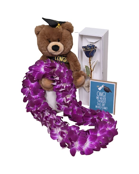 The Grad Era Bundle - A playful, school-spirited gift set centered on a soft brown teddy bear wearing a graduation cap and sash, paired with a long bombay orchid lei draped proudly around the front-perfect as a graduation gift or a "just because" surprise to celebrate a milestone. The strong purple-and-blue palette feels celebratory and sentimental, the kind of present that will make the person you're thinking of feel seen and celebrated on their big day.  Beside the bear is a tall white presentation box holding a single preserved blue rose that will never die, creating a lasting moment your grad can keep on display. A small congratulatory greeting card completes the ensemble, blending plush comfort with keepsake florals. This set reads as a thoughtful graduation gift that also works beautifully for sending congratulations or a spontaneous "thinking of you" sentiment any time of year.