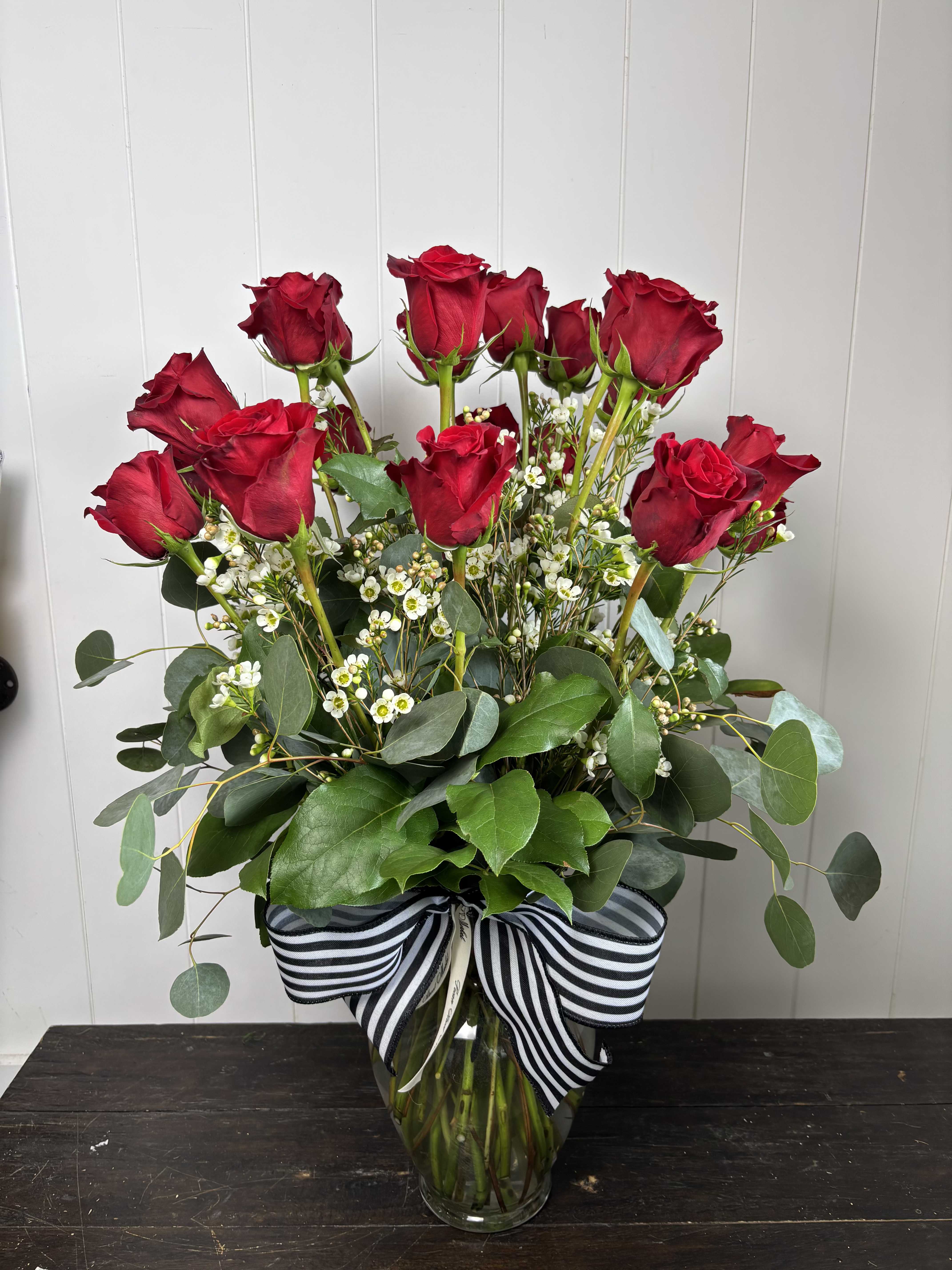 Red roses arranged in a clear glass vase with a striped ribbon.