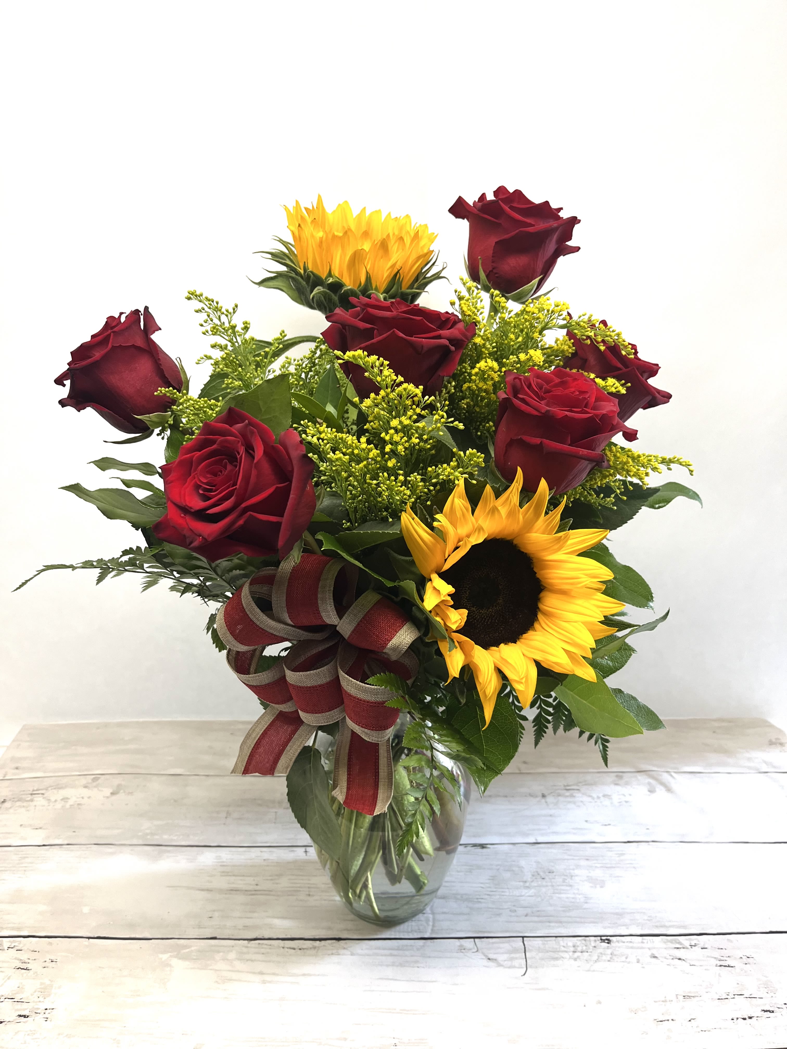 Bouquet of red roses and sunflowers in a glass vase with a ribbon