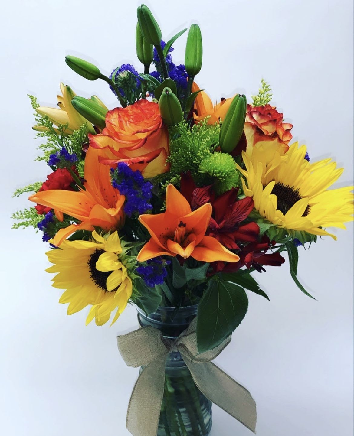 Colorful bouquet with sunflowers, lilies, and roses in a glass vase