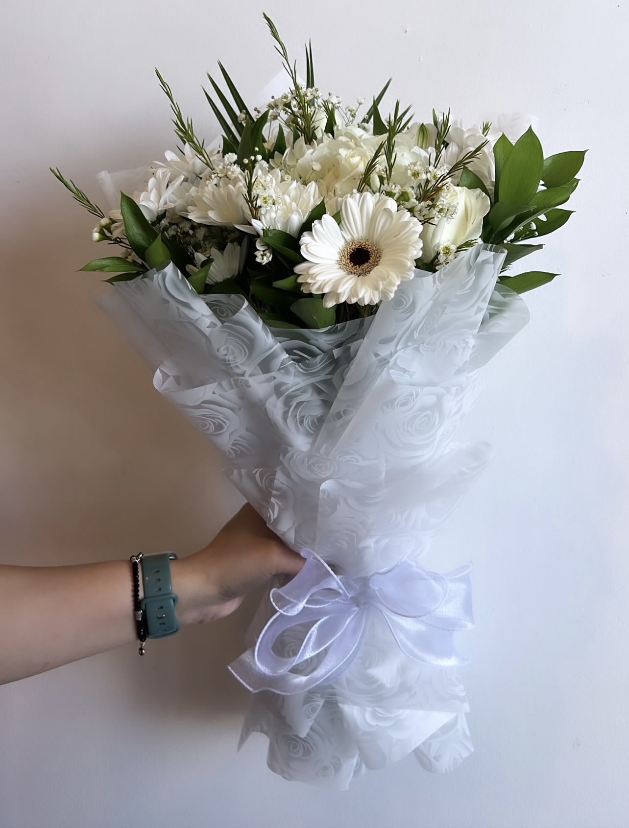 White bouquet with gerbera daisies and roses wrapped in sheer ribboned paper