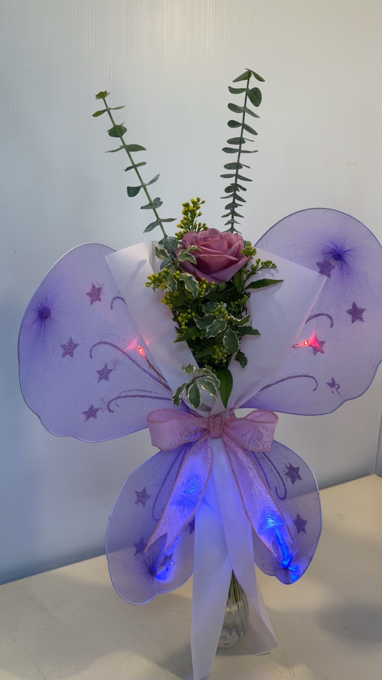 Dance LED Light Up Butterfly Wrap - A rose or Gerber accented with fresh greenery, filler, and sparkling butterfly wings that light up. Perfect for dance recitals!