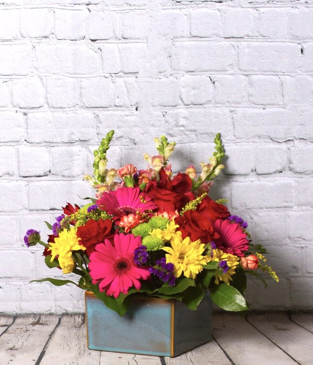 Bright mixed flower arrangement in a square blue vase