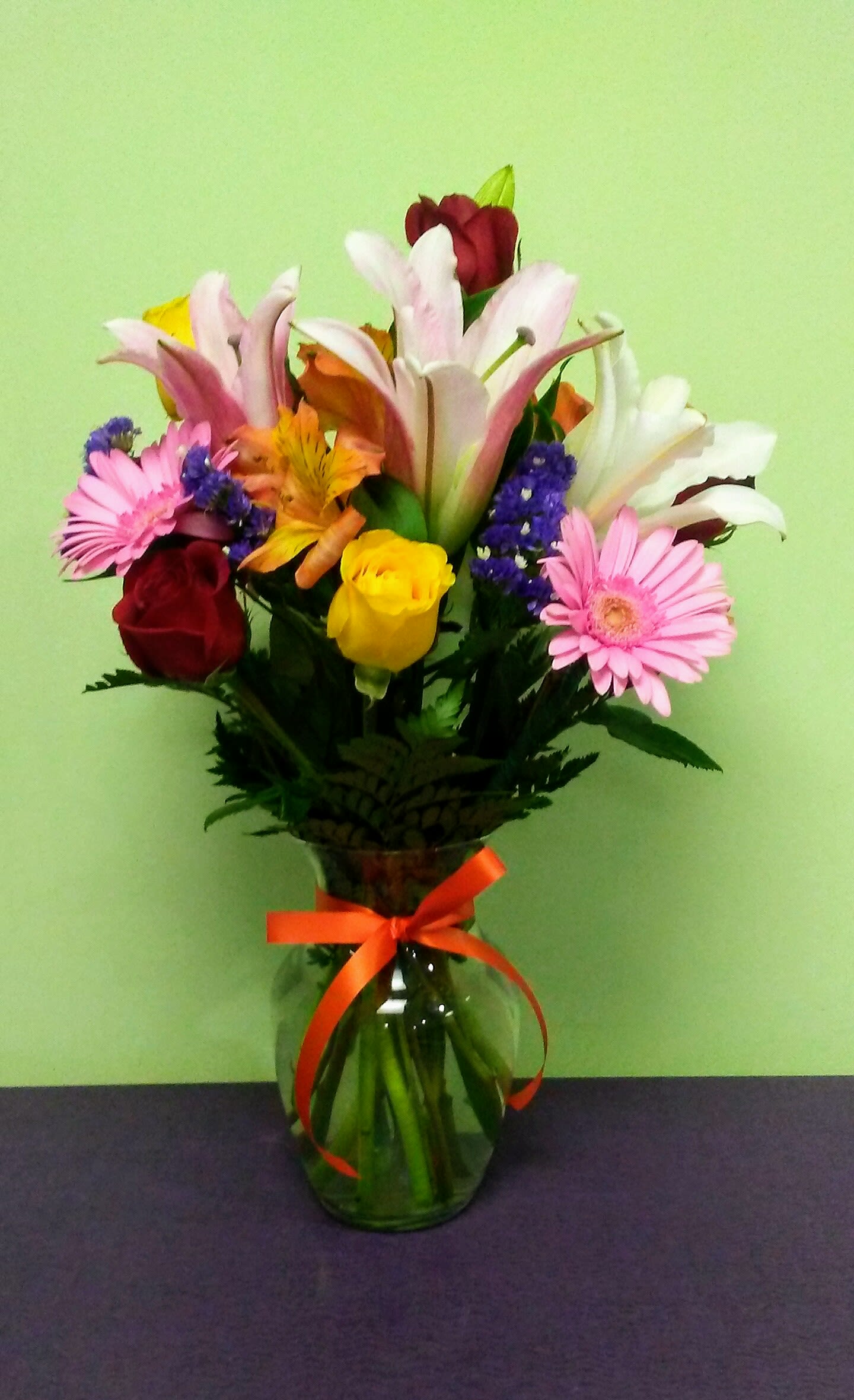 Mixed bouquet of lilies, roses, and daisies in a glass vase with a ribbon
