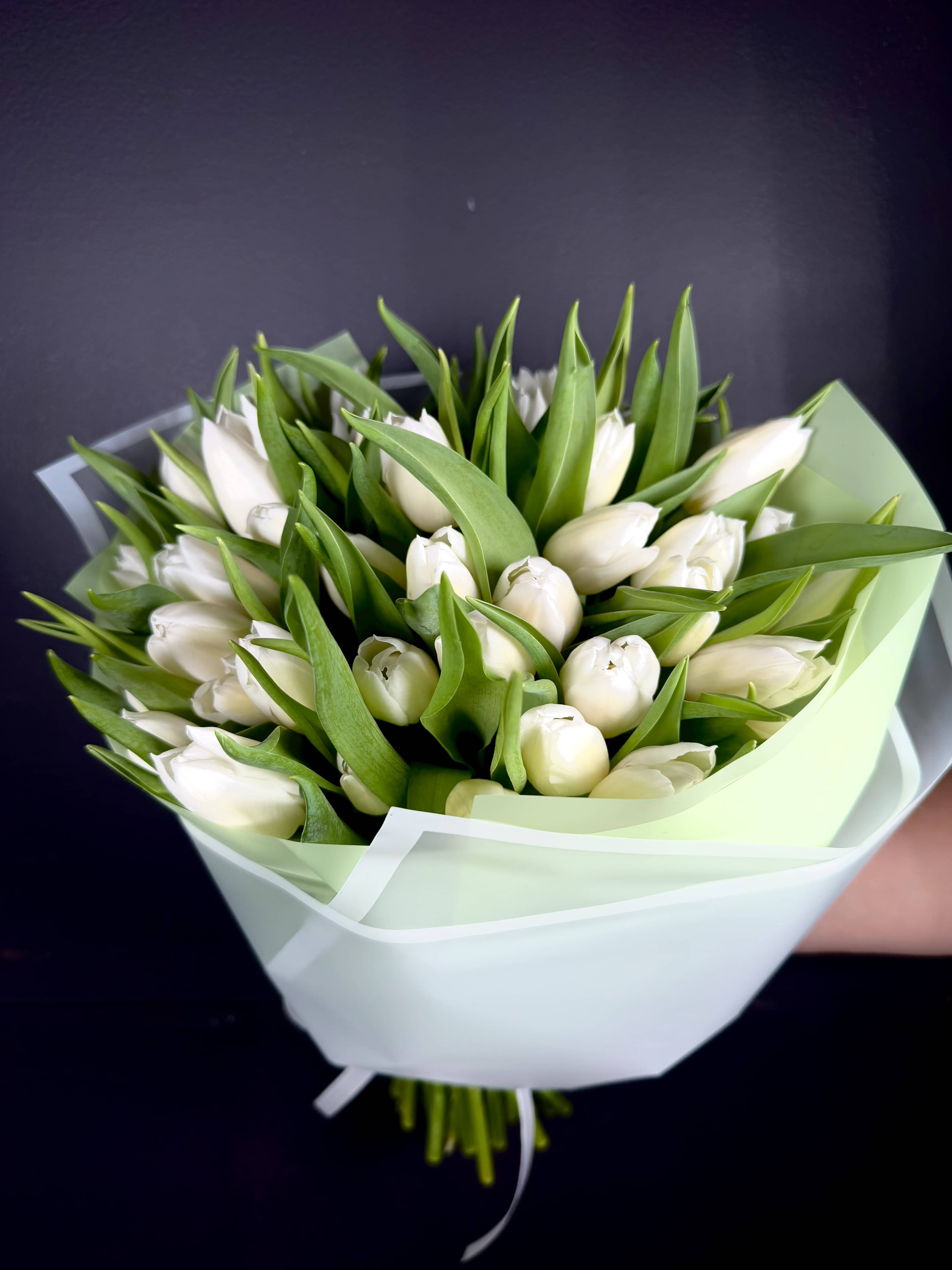 Bouquet of white tulips wrapped in pale green and white paper