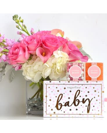 Pink roses and white hydrangeas in a glass vase with baby gift boxes