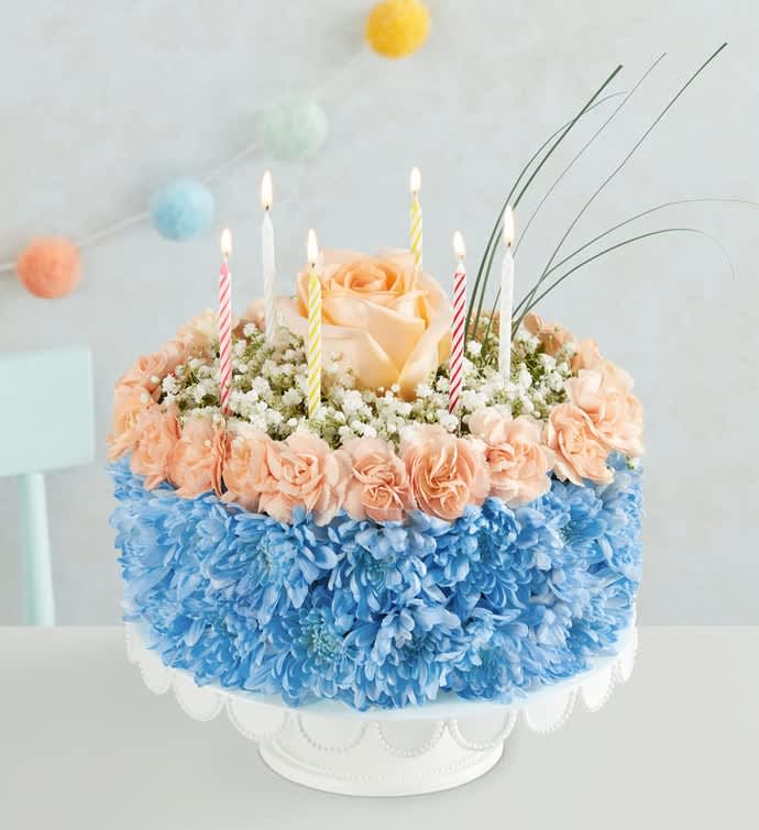 Round floral cake with candles and peach roses on a white stand