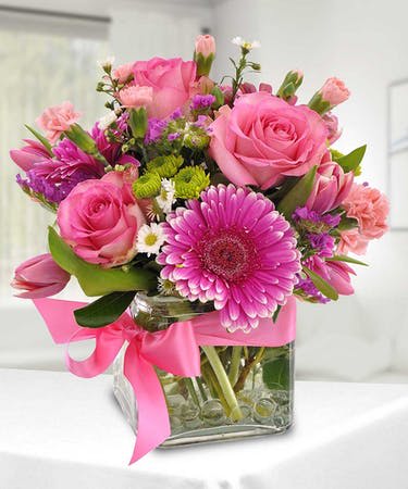 Perfectly Pink - We have designed a perfectly pink arrangement using roses, mini carnations, Gerbera daisies, button mums and fillers with clear gemstones inside a cube vase with a lovely satin pink bow.