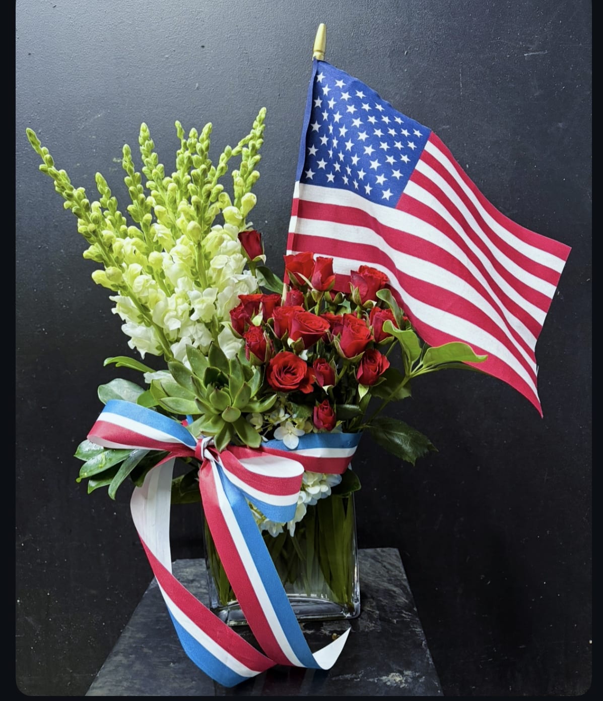 Fourth of July - Red, white, and blue! Snap dragons, spray roses, succulent, hydrangea We use flowers that are available at that given time. The look and the freshness of the flowers are always the most important. Subs may be made based on best product available.