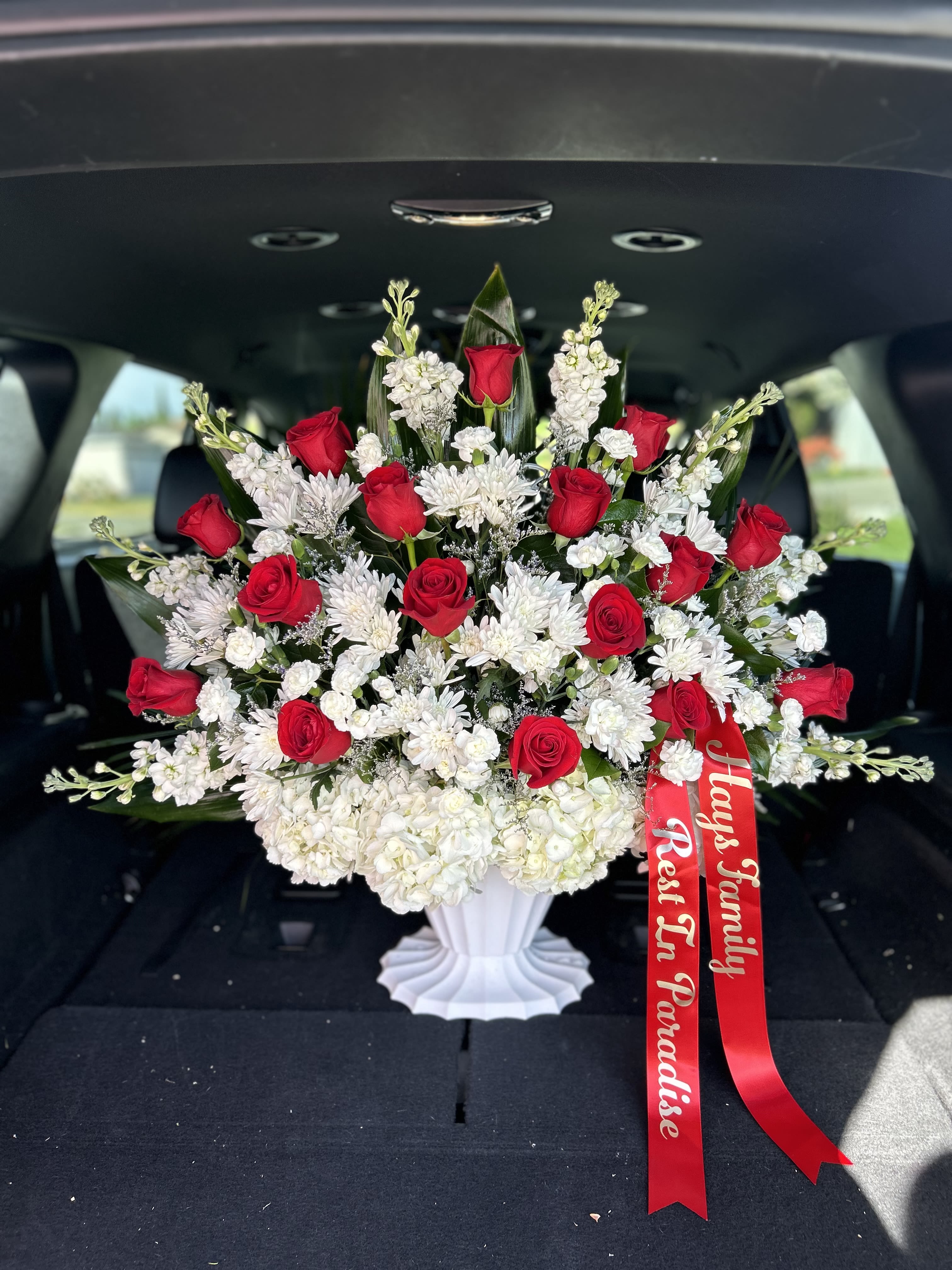Red roses and white flowers arranged in a white vase with a red ribbon