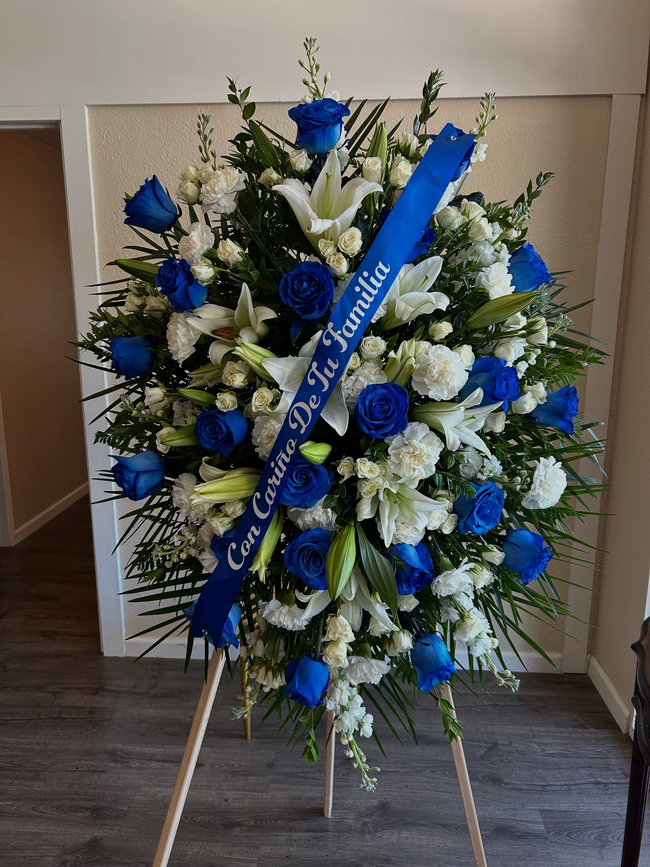 Large blue and white funeral spray on an easel with a ribbon