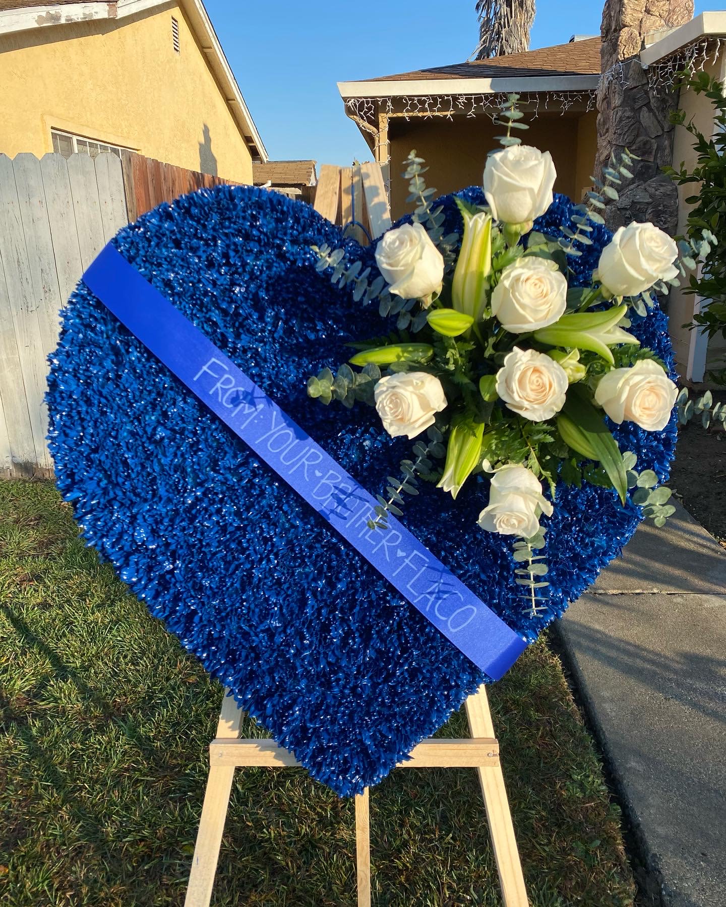 Blue heart-shaped floral tribute with white roses and lilies on an easel