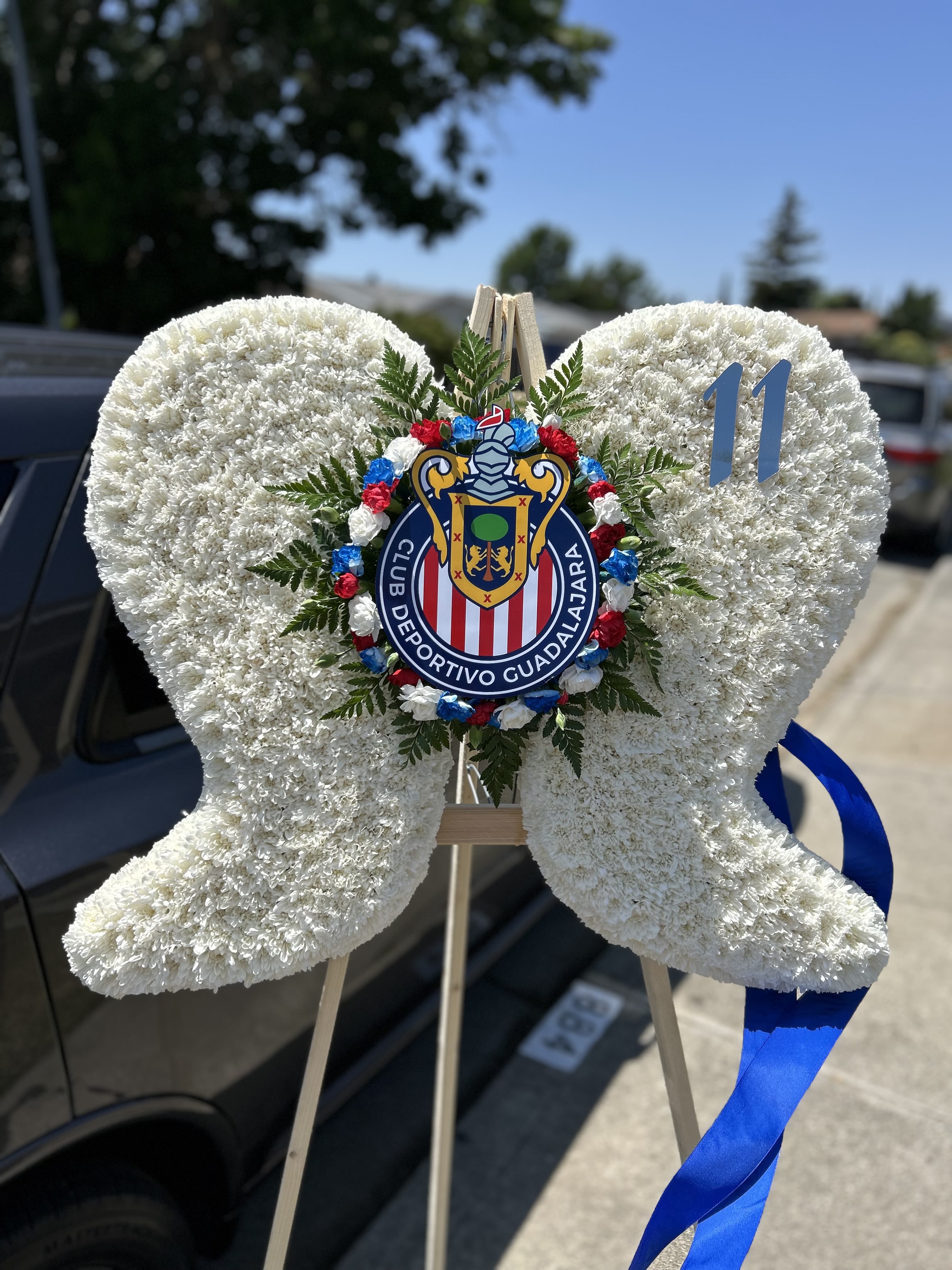 White floral heart wreath on a stand with a sports club emblem