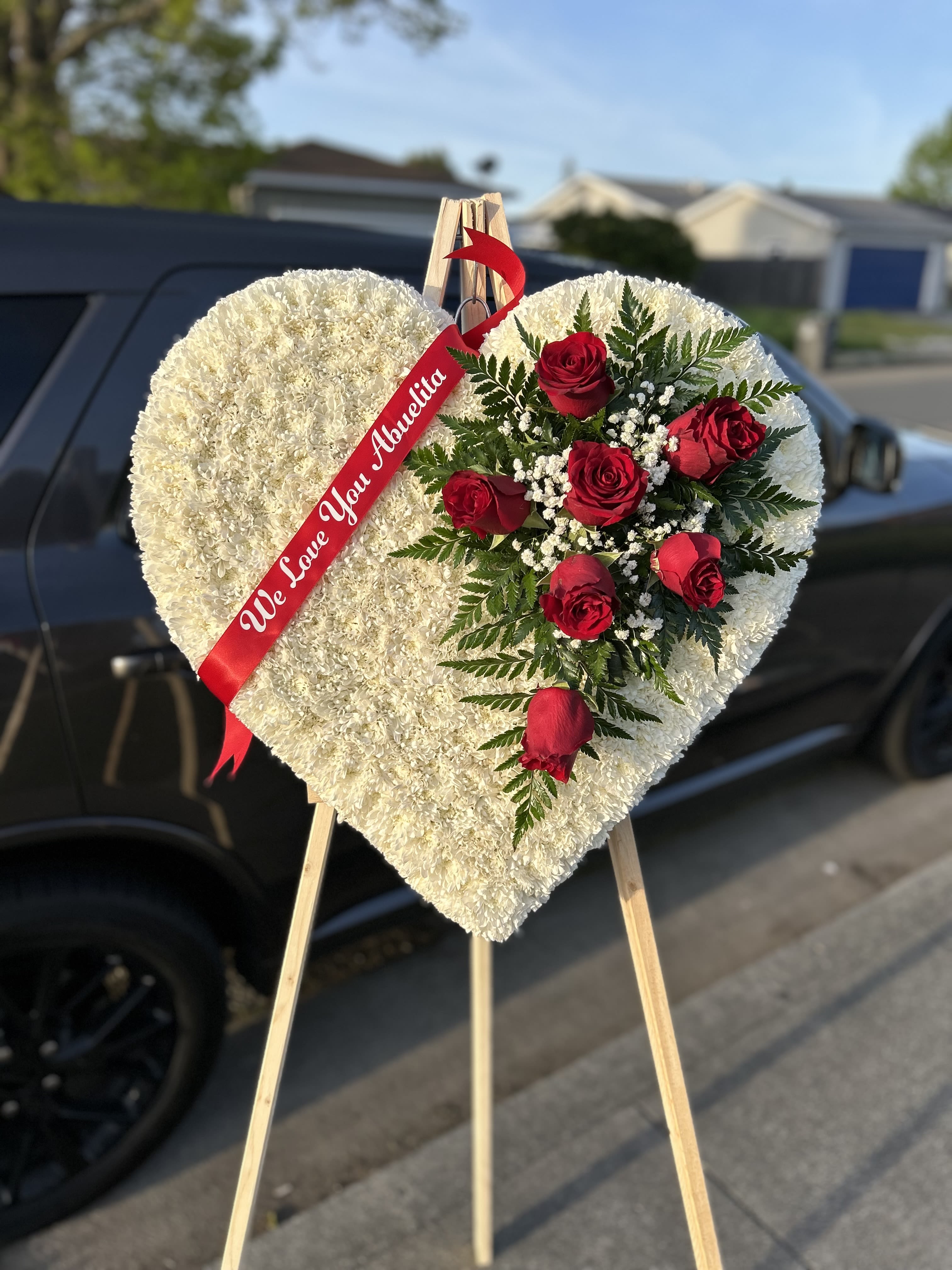 Heart-shaped white floral tribute with red roses on an easel