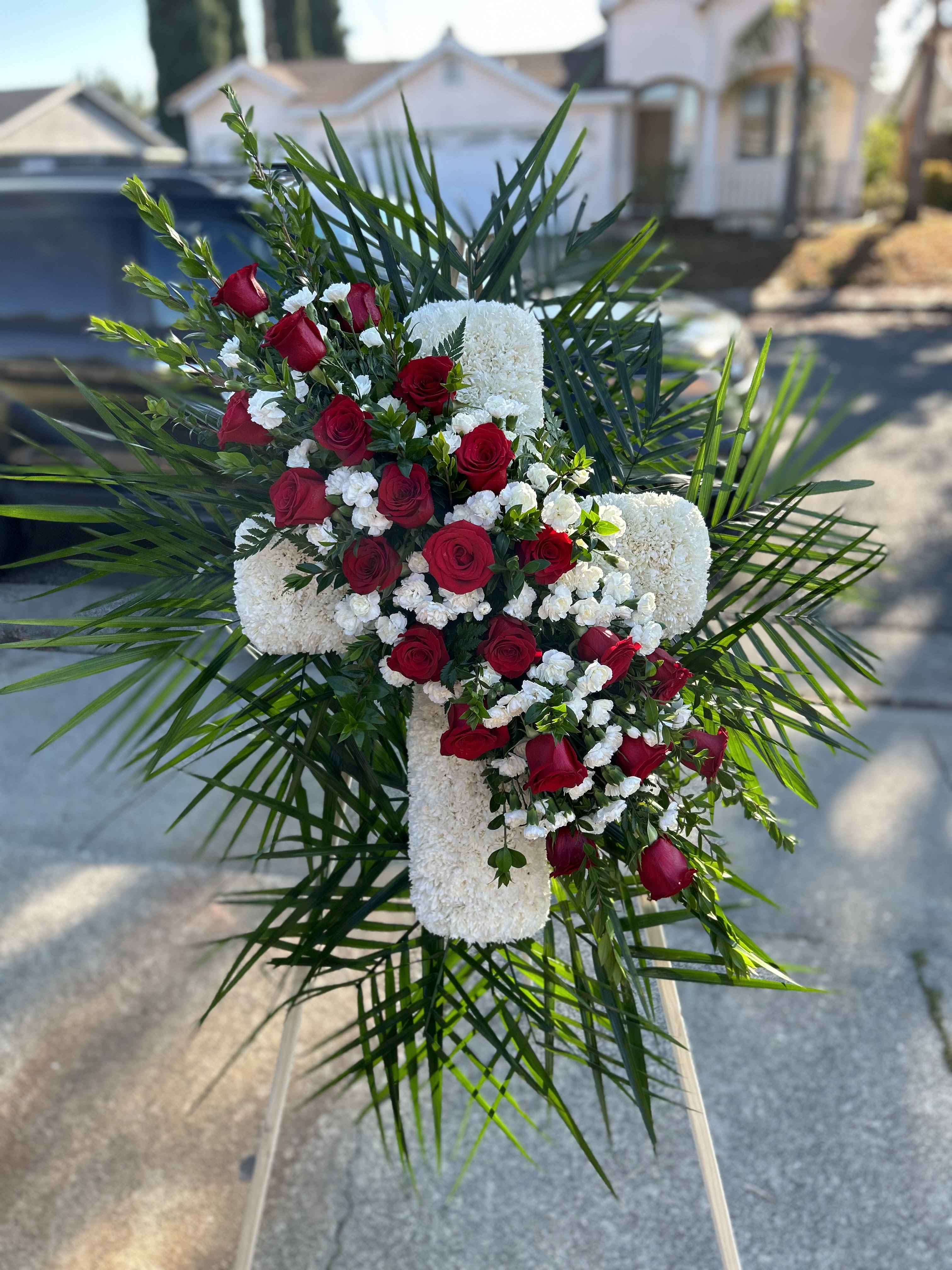 Red roses and white flowers arranged in a cross on an easel