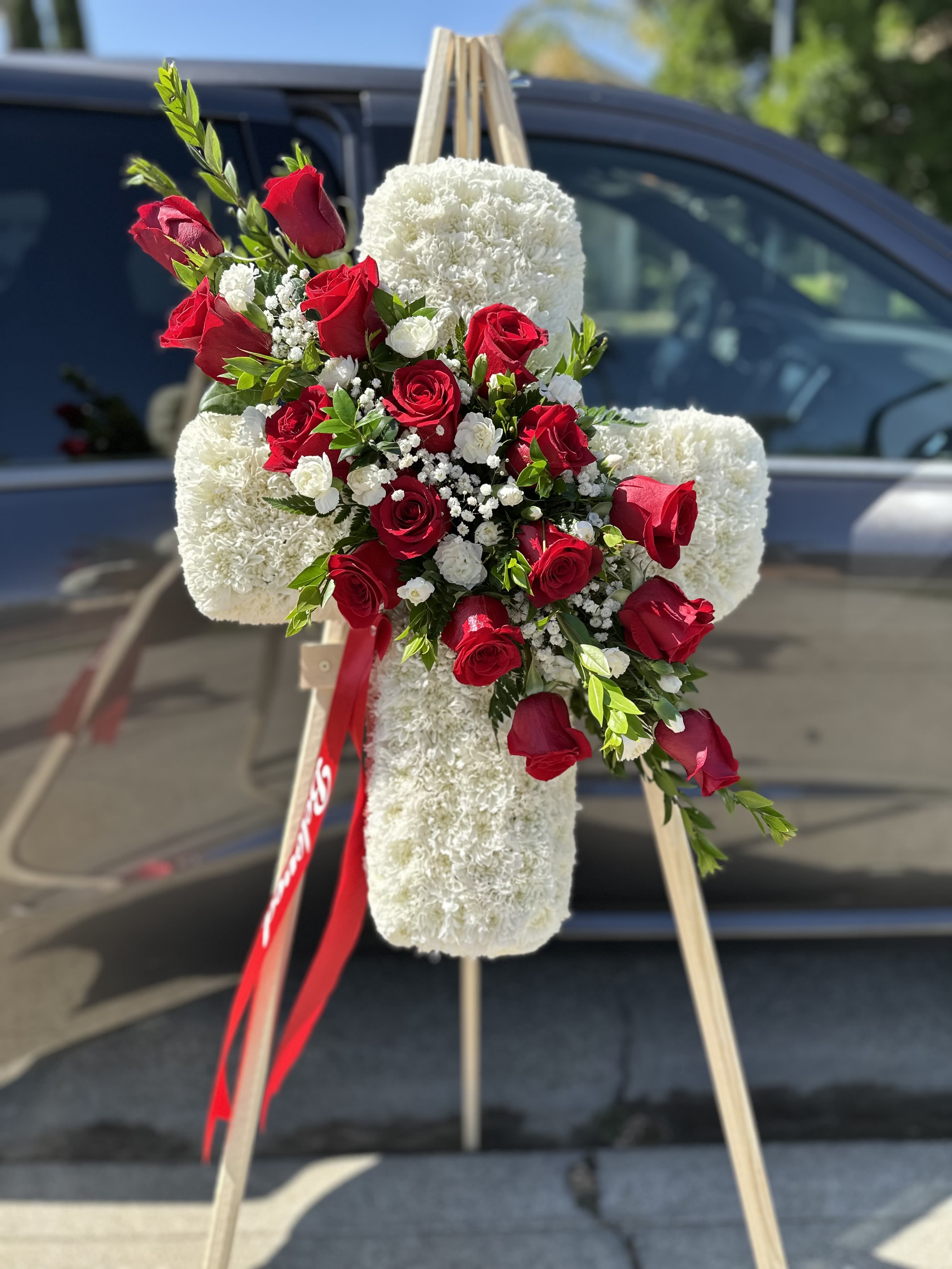 Red roses arranged on a white floral cross on an easel