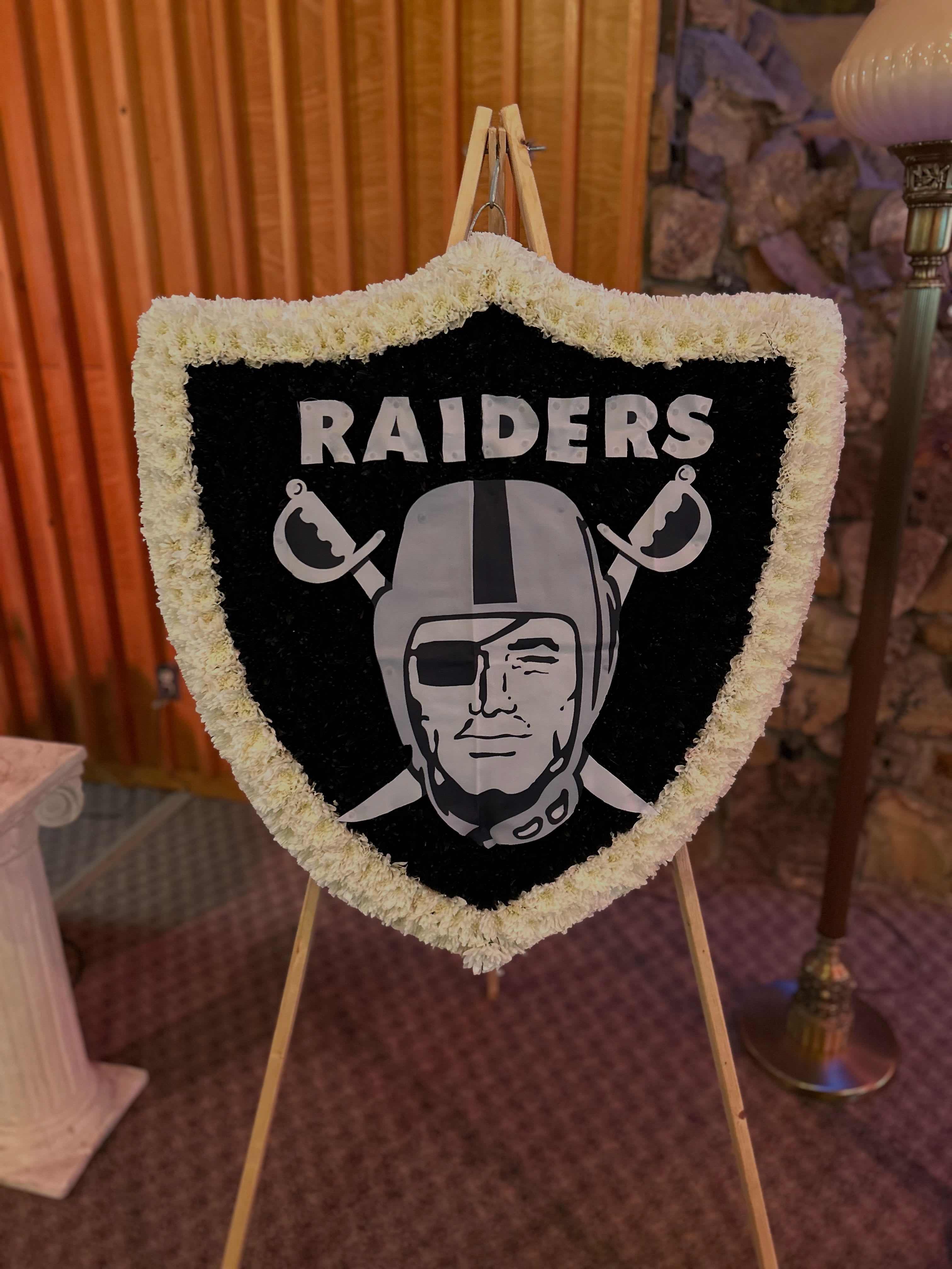 Shield-shaped floral tribute with a Raiders logo on an easel