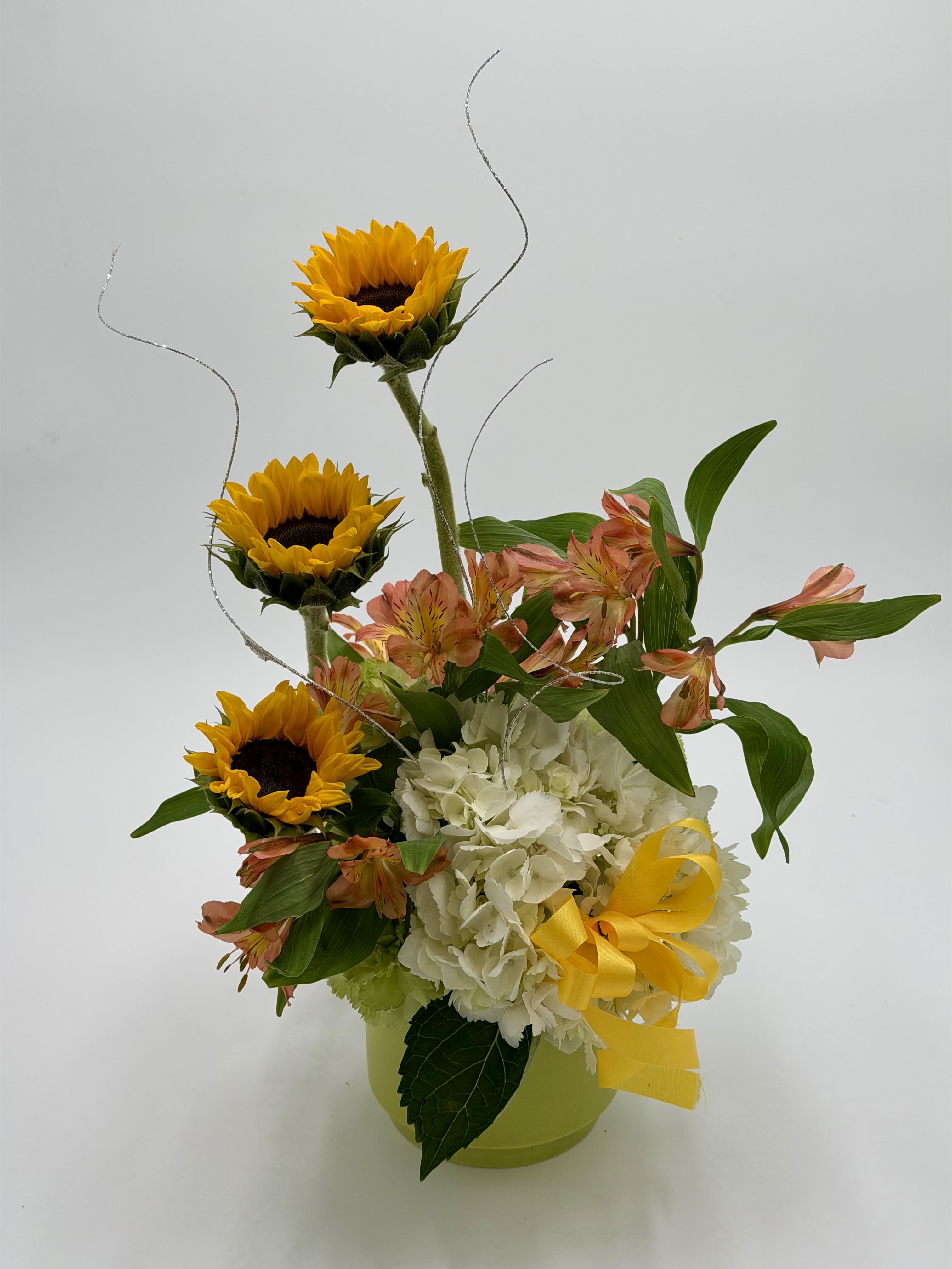 Sunshine and Grace - Sunshine and Grace is a cheerful arrangement that brings warmth and elegance together in one radiant design. Bright sunflowers rise above soft white hydrangea and delicate peach alstroemeria, creating a beautiful balance of bold color and gentle charm. Designed in a keepsake container with flowing accents and a sunny ribbon, this arrangement is perfect for celebrating life’s happiest moments.