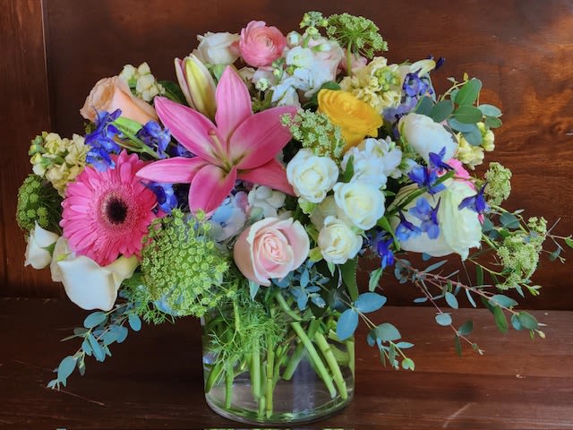 Mixed bouquet of pink, white, yellow, and blue flowers in a glass vase