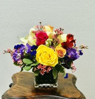 Colorful bouquet of roses and mixed flowers in a square glass vase