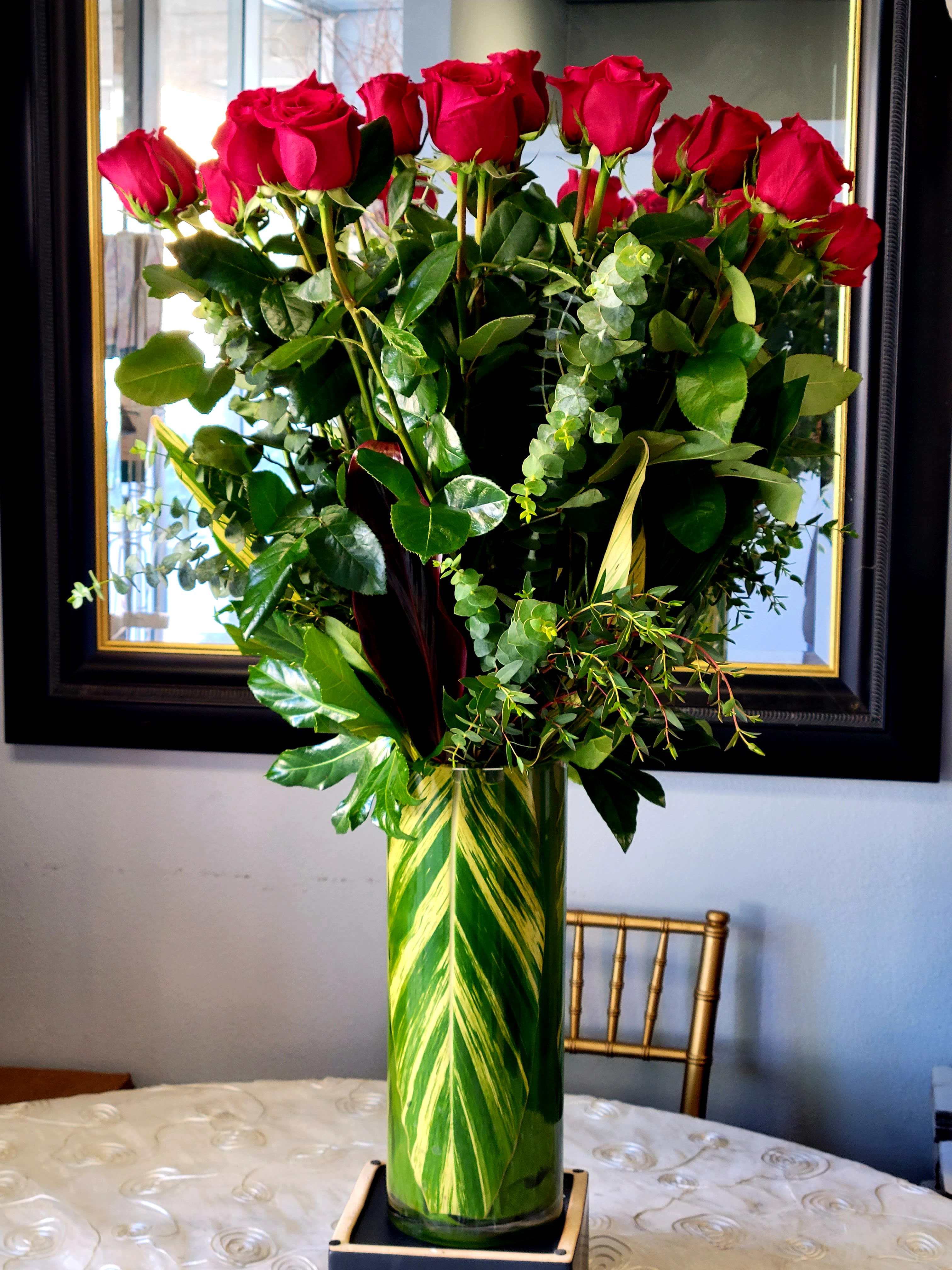 Tall vase arrangement of red roses with mixed greenery