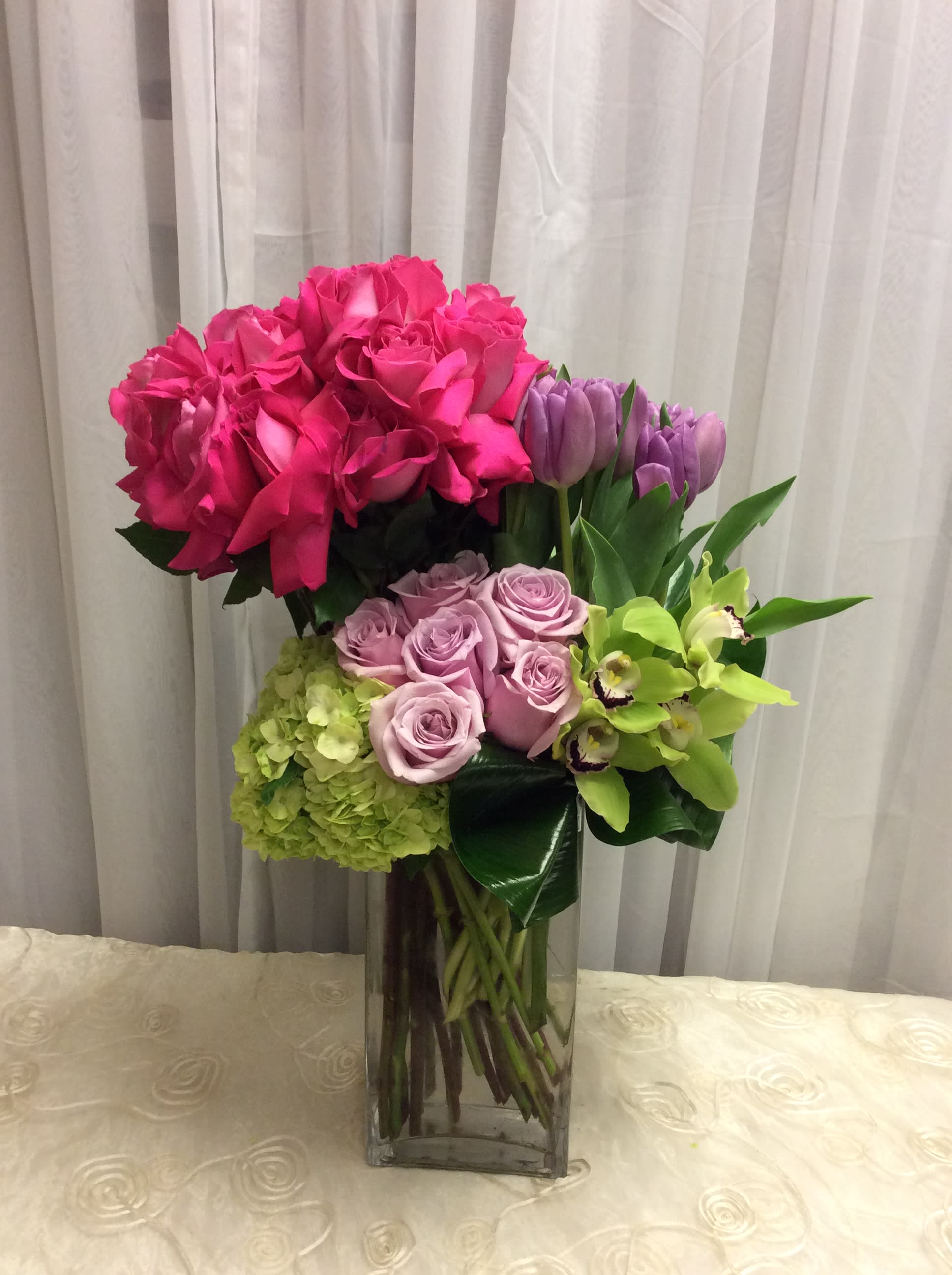 Pink roses, lavender roses, tulips, hydrangea, and green orchids in a glass vase