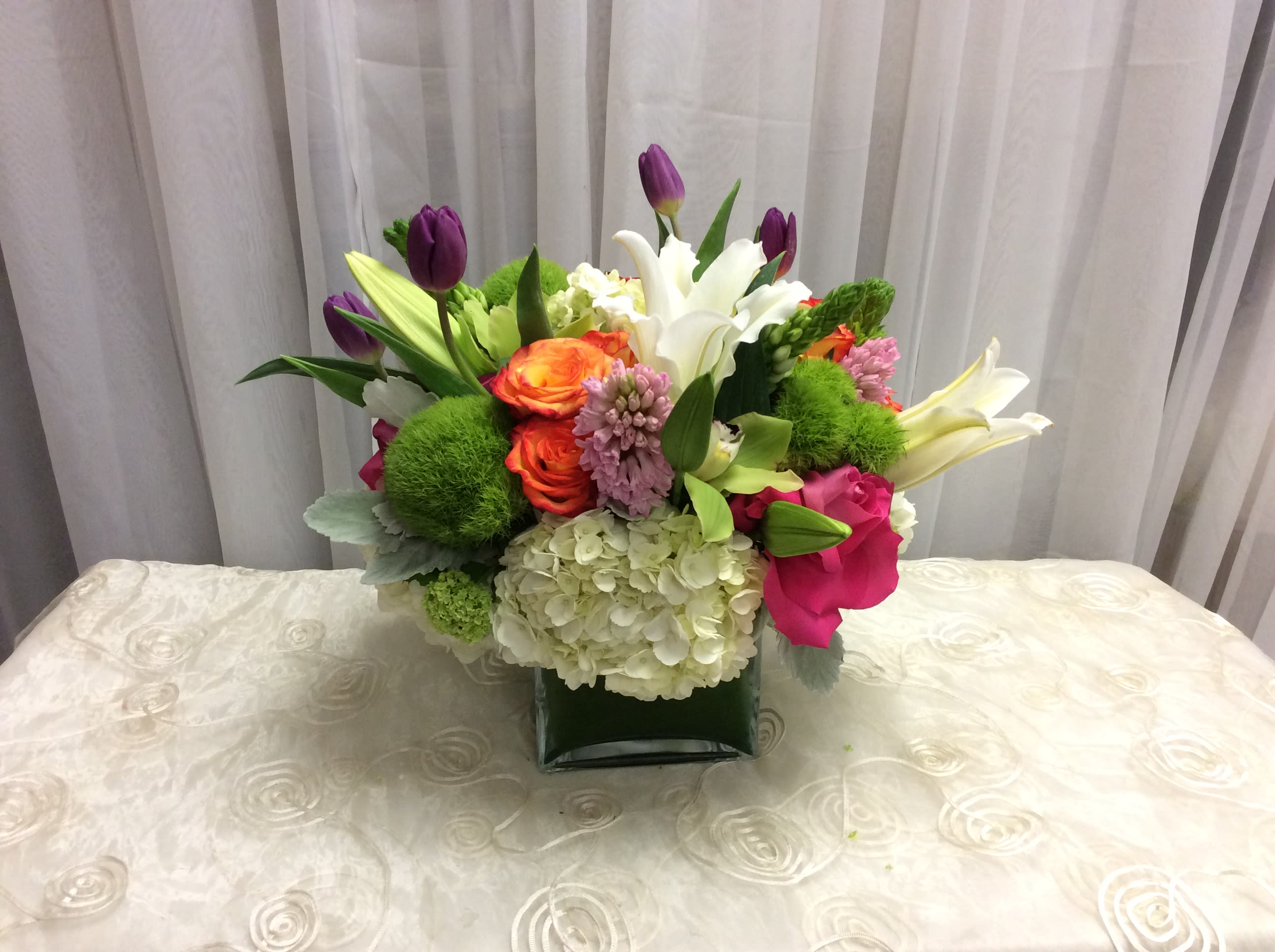 Mixed bouquet with lilies, tulips, roses, and hydrangea in a square vase