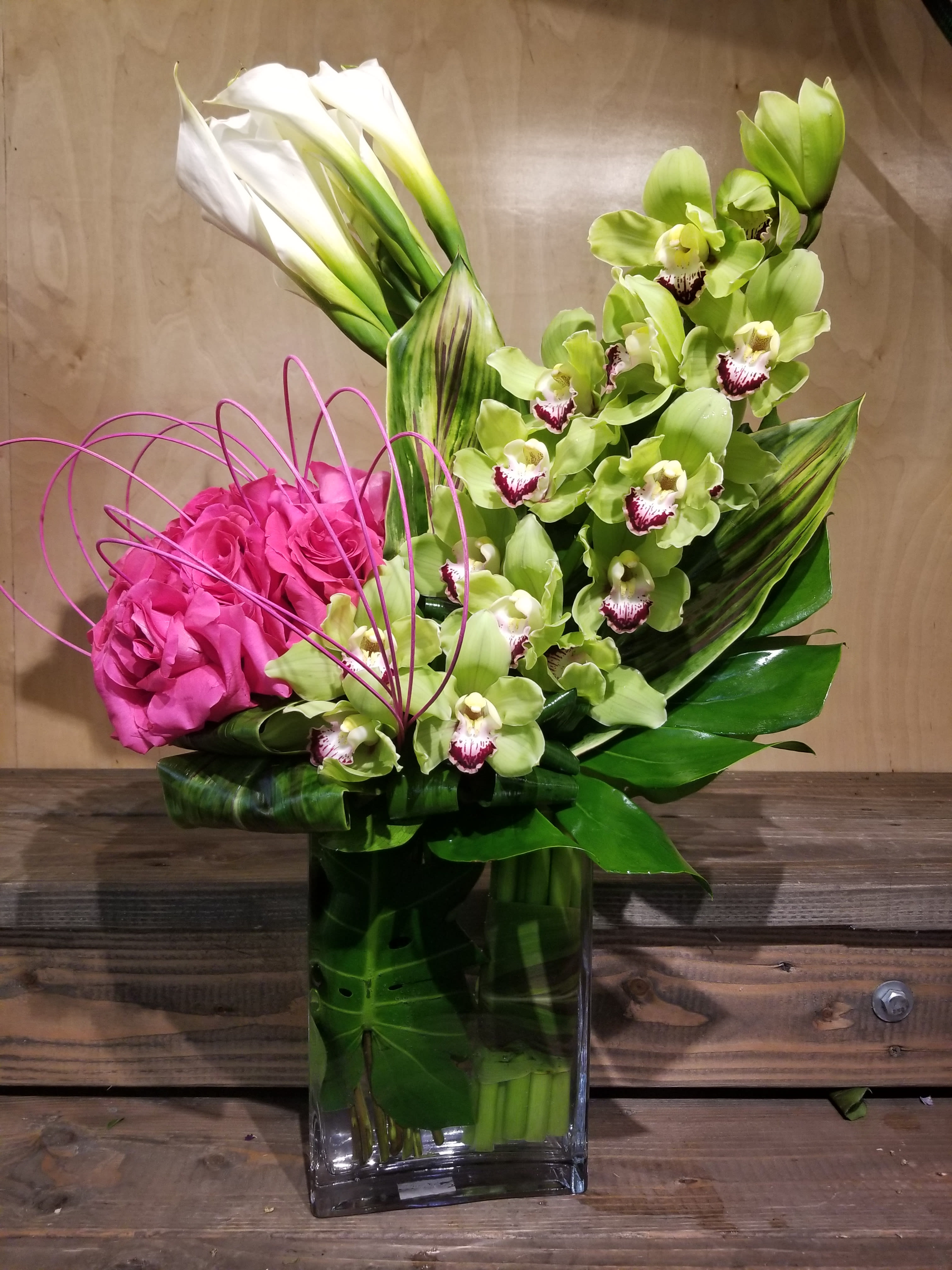 Pink roses and green orchids in a tall glass vase with white calla lilies