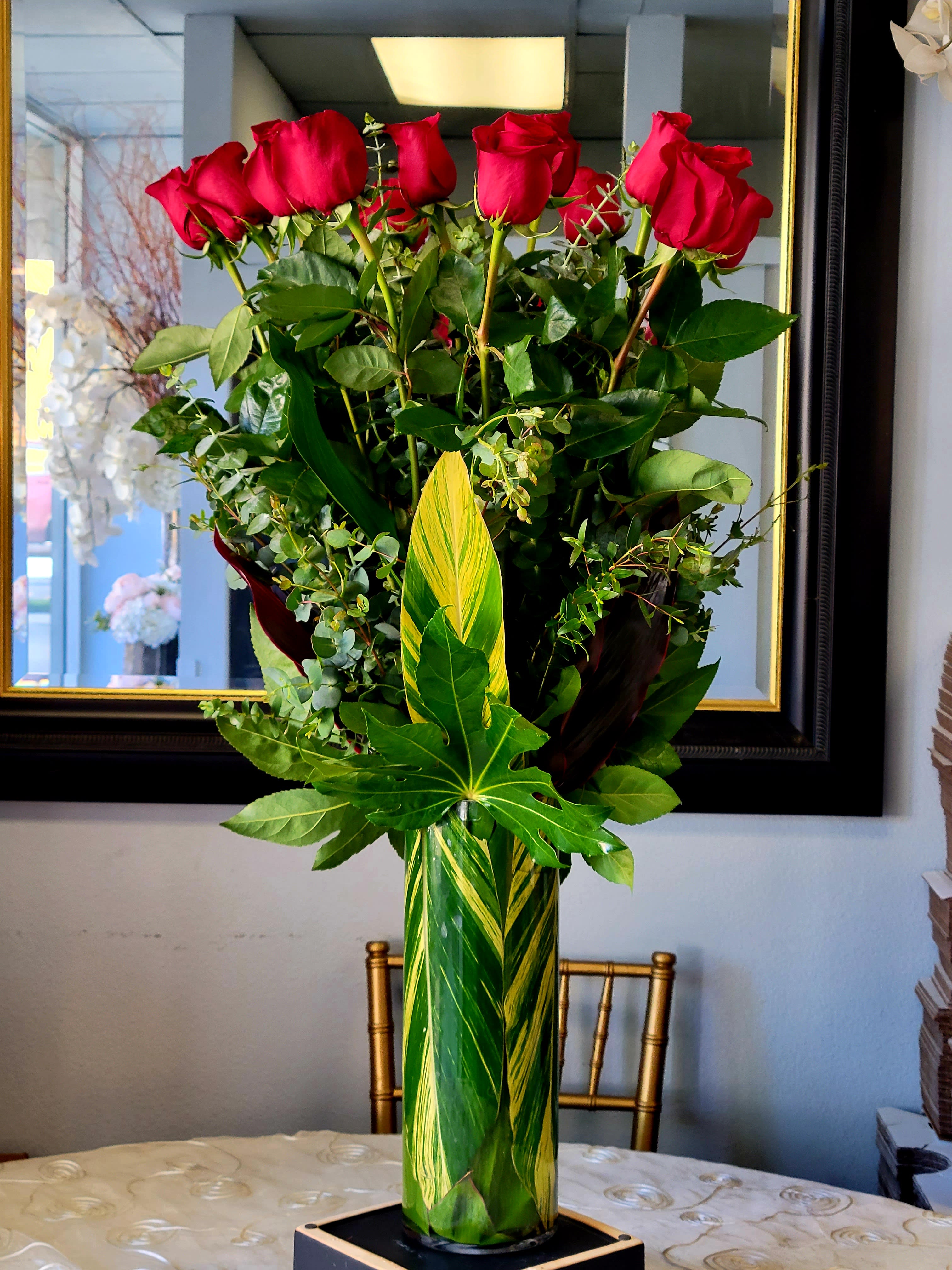 Tall vase arrangement of red roses with mixed greenery