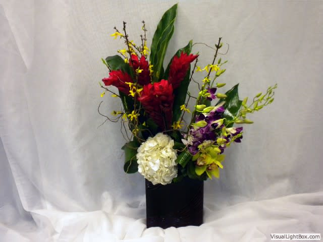 Tropical floral arrangement with red and purple blooms in a black vase