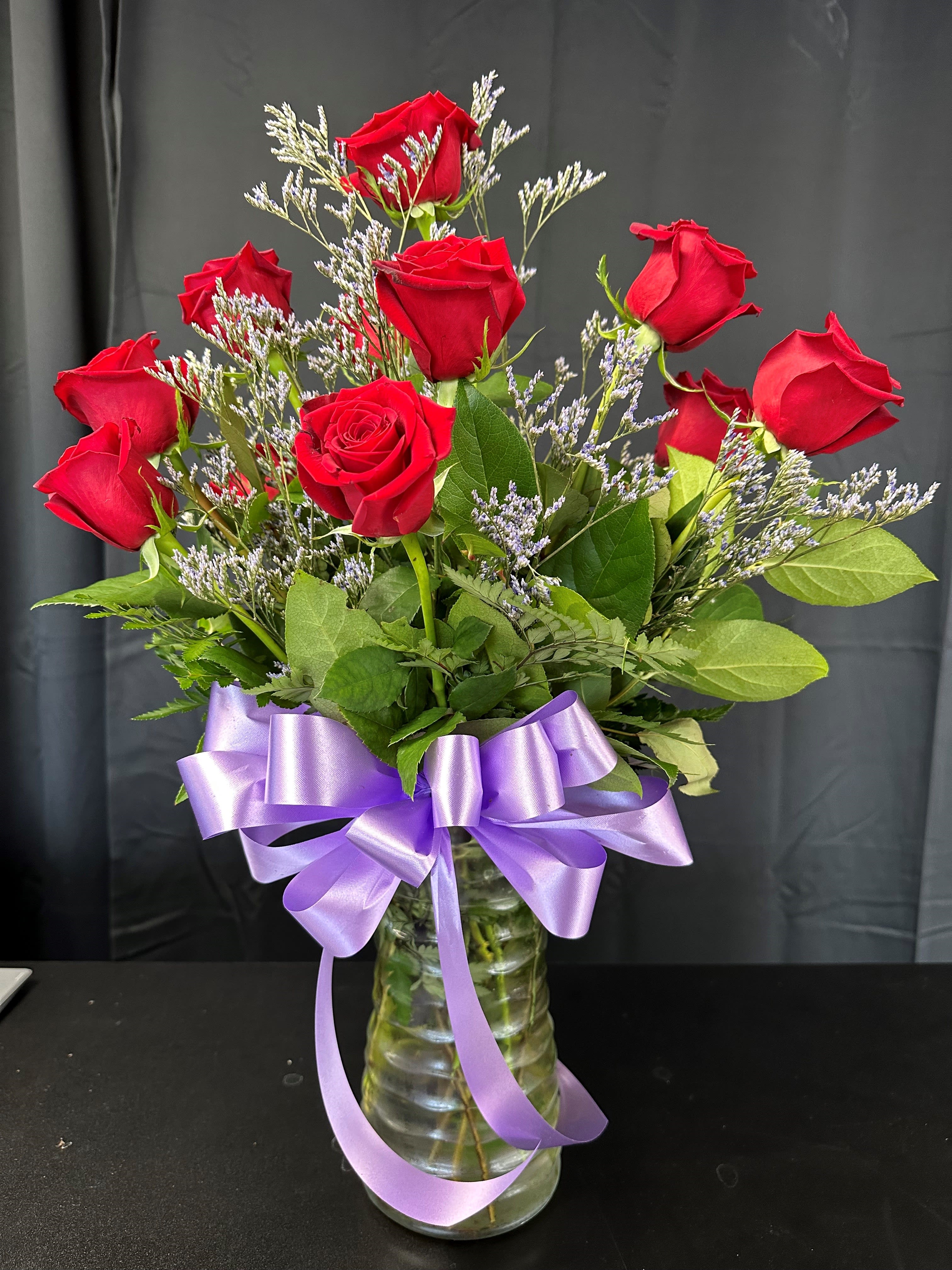 Red roses in a glass vase with a purple ribbon