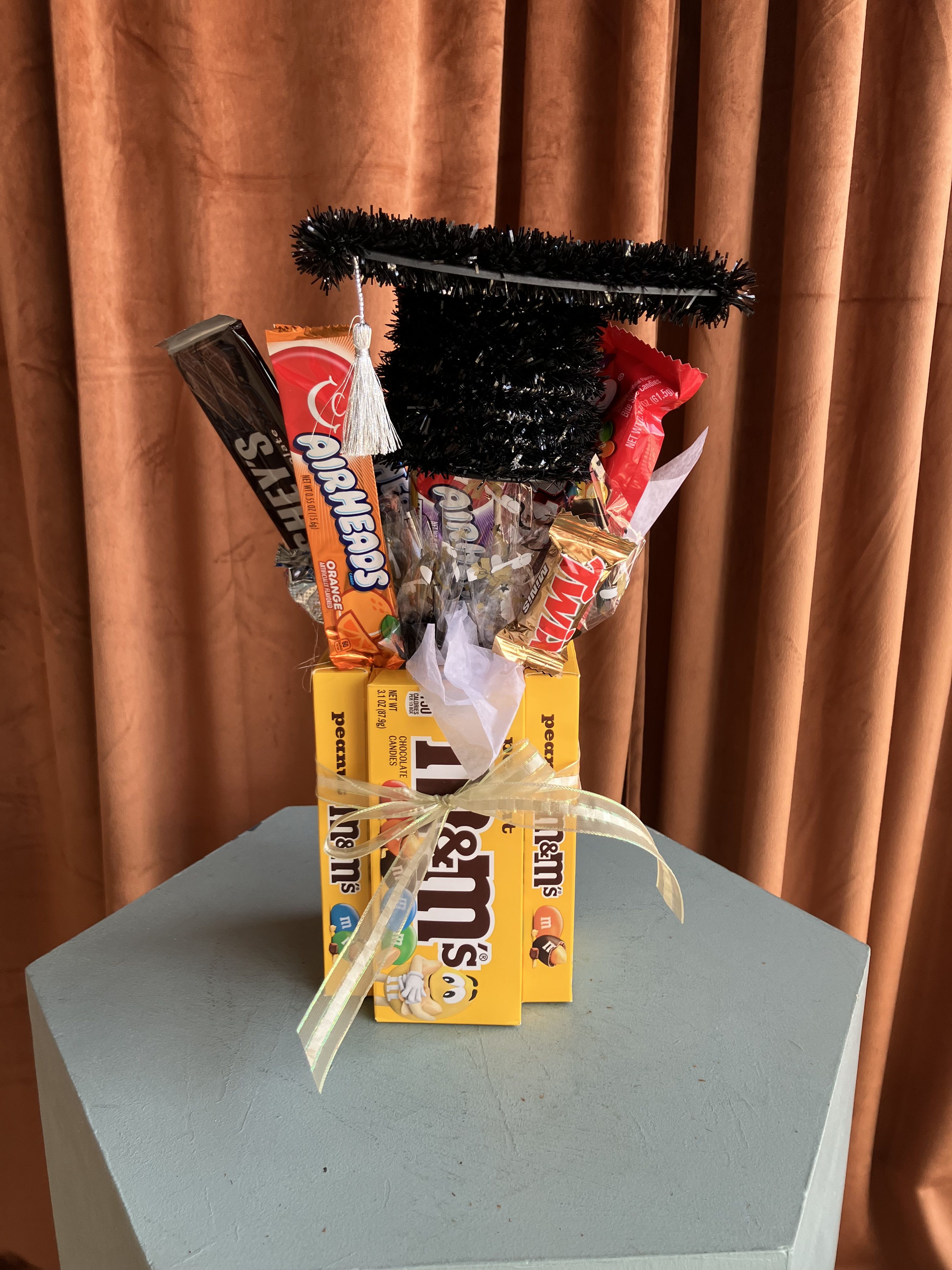 Graduation Candy Bouquet - Our Graduation Candy Bouquet is packed with a playful mix of candies arranged in a keepsake graduation-themed design, complete with a festive grad cap topper. Perfect for graduation parties, graduations, and senior milestones.   Each bouquet is uniquely designed and candy selections will vary based on availability, making every arrangement one-of-a-kind while keeping the same fun and colorful style.