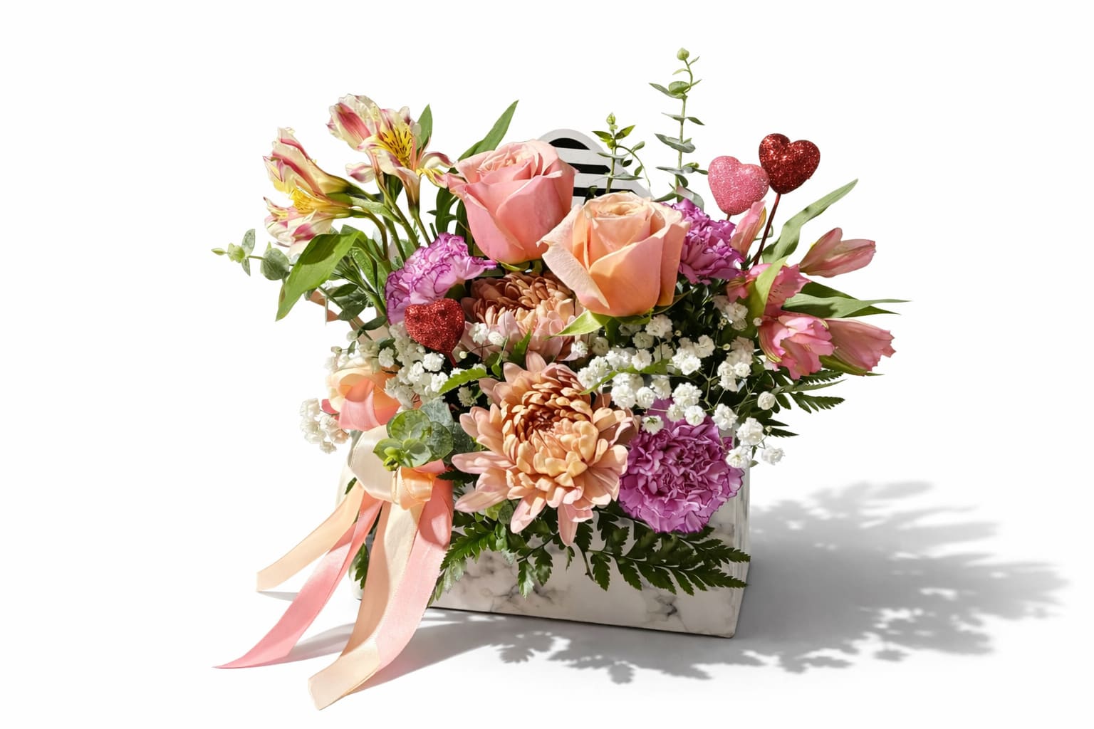 Mixed bouquet of pink and peach flowers in a marble box with heart picks