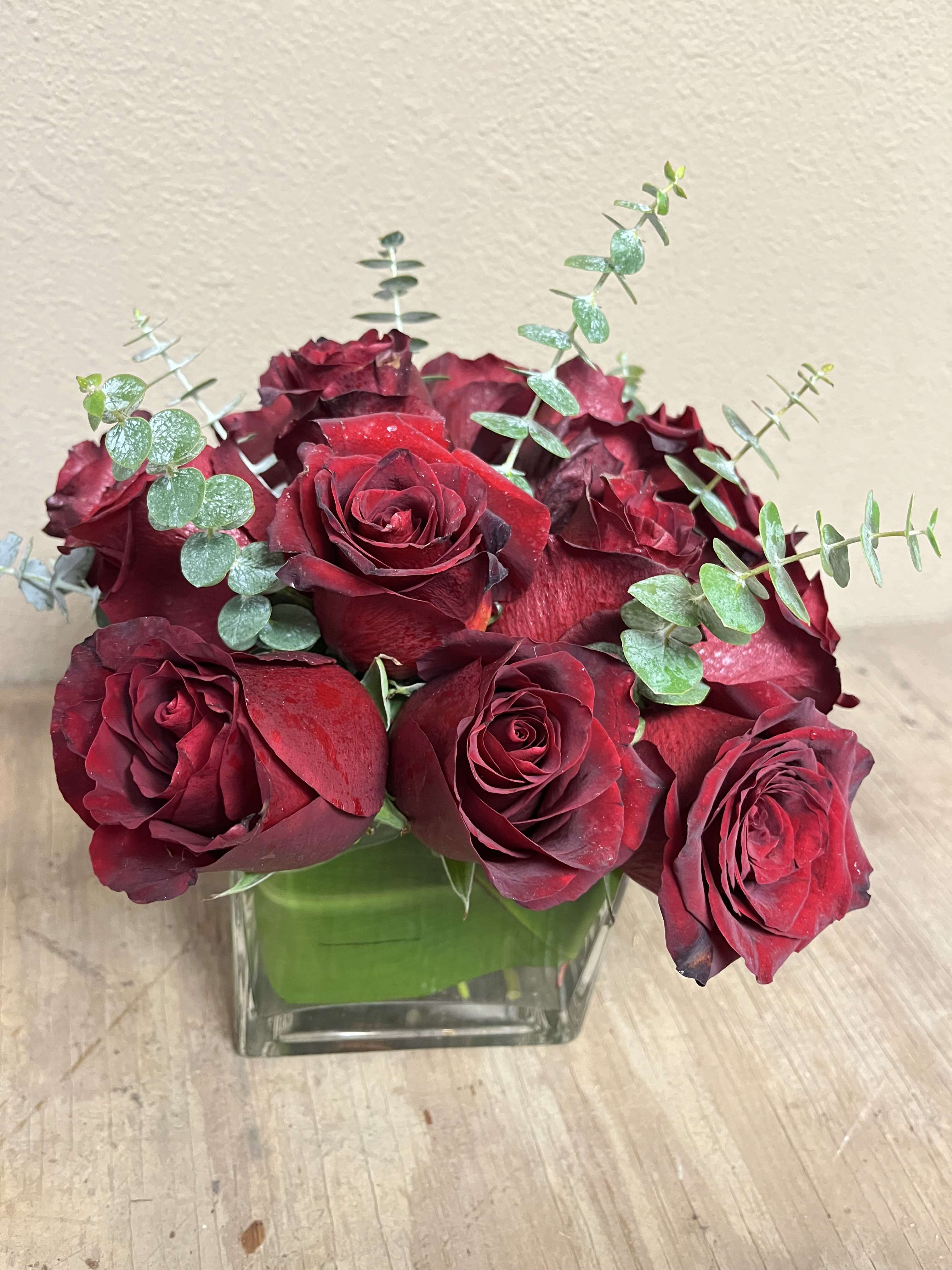 Red roses arranged in a square glass vase with eucalyptus stems