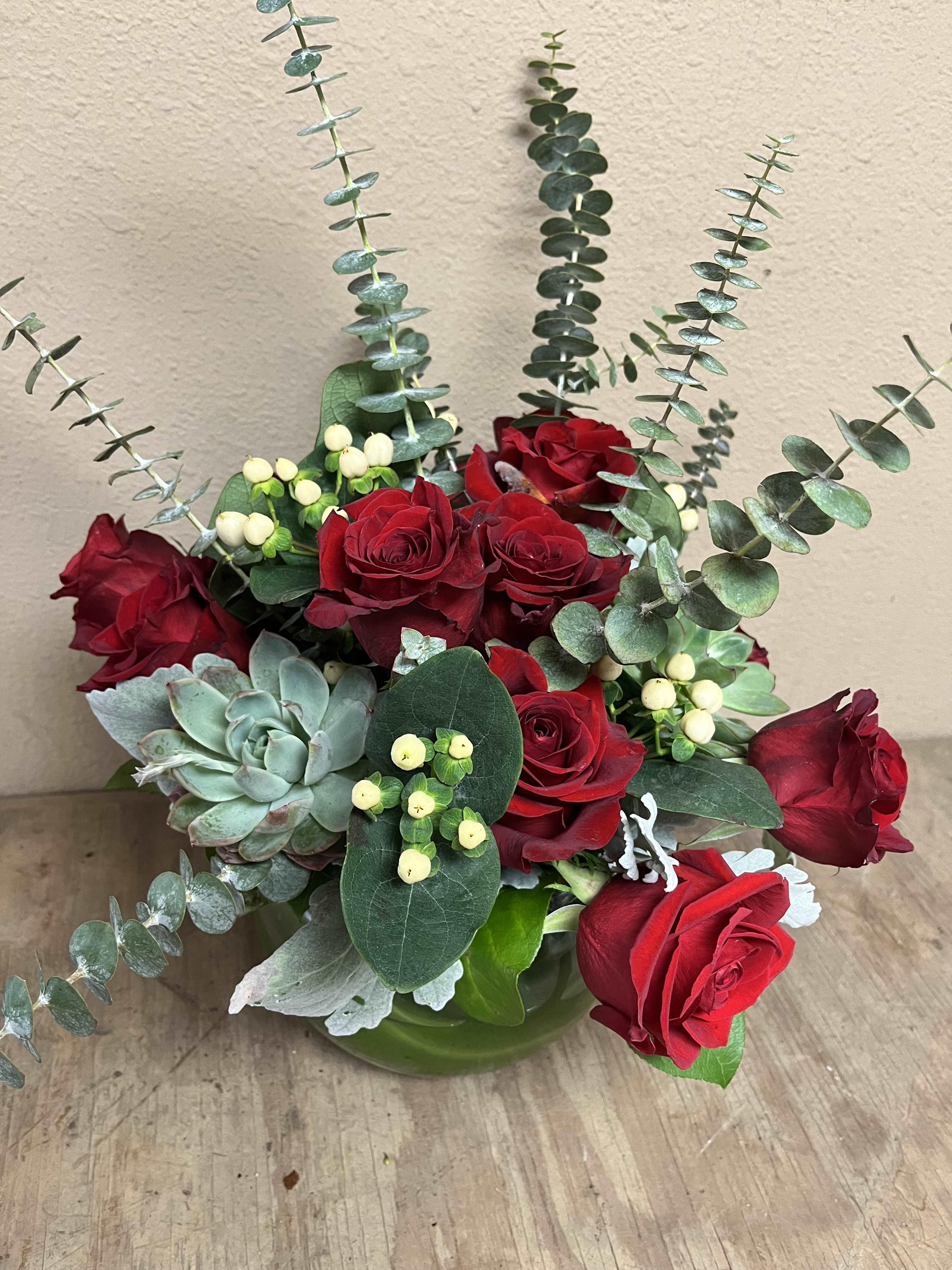 Red roses arranged with eucalyptus and a succulent in a green vase