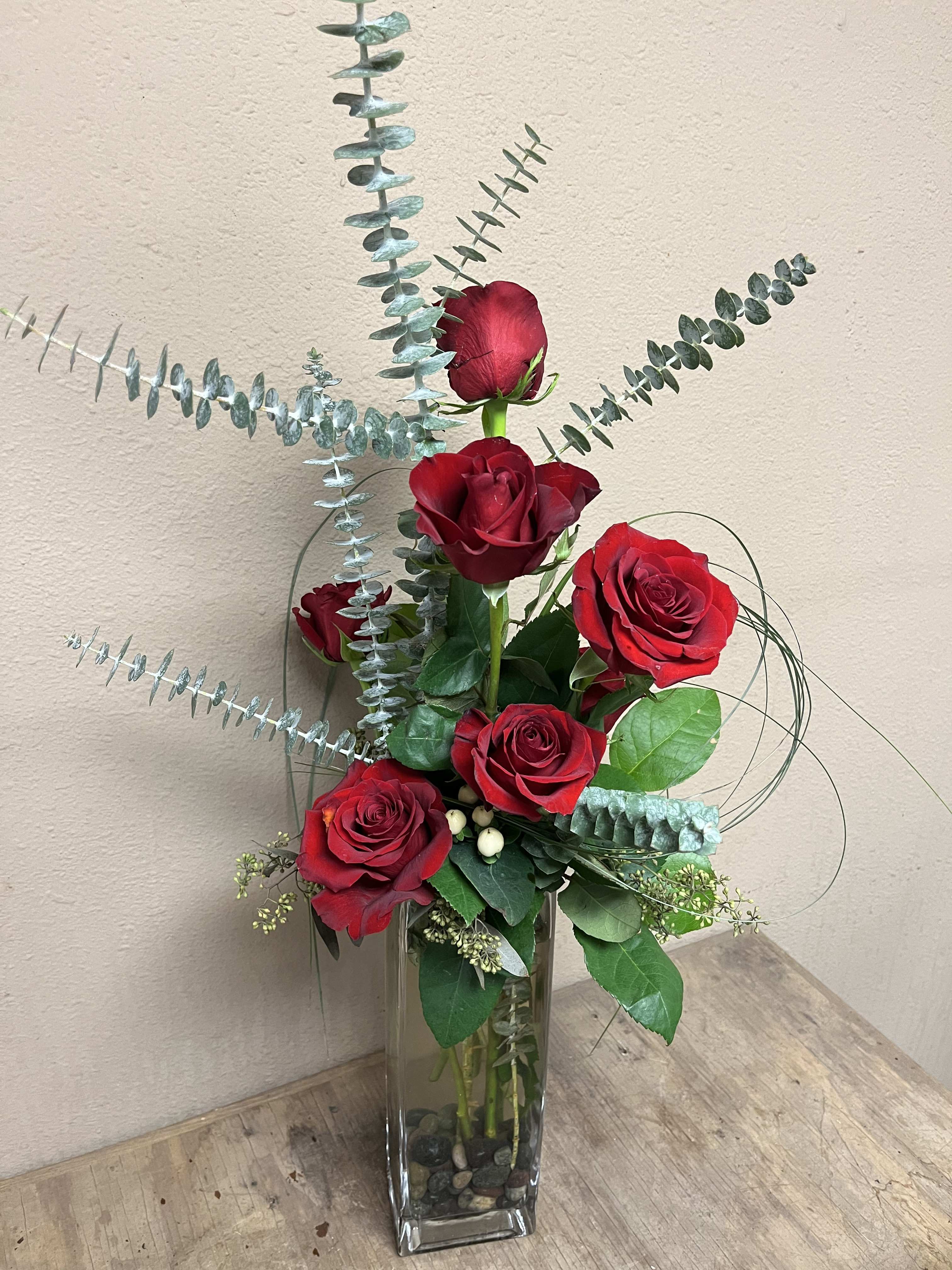 Red roses in a tall glass vase with eucalyptus stems
