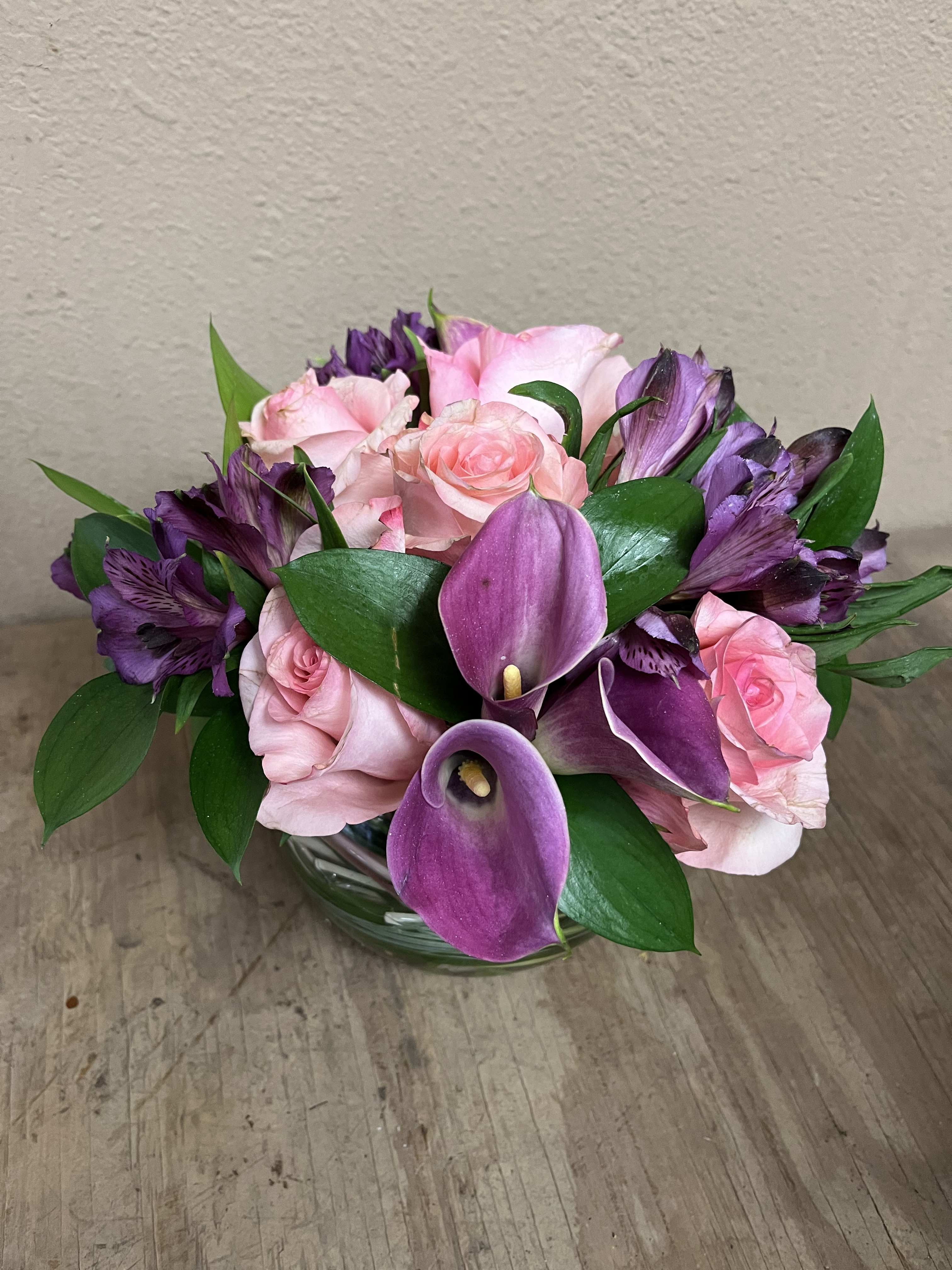 Pink roses and purple calla lilies in a glass bowl vase