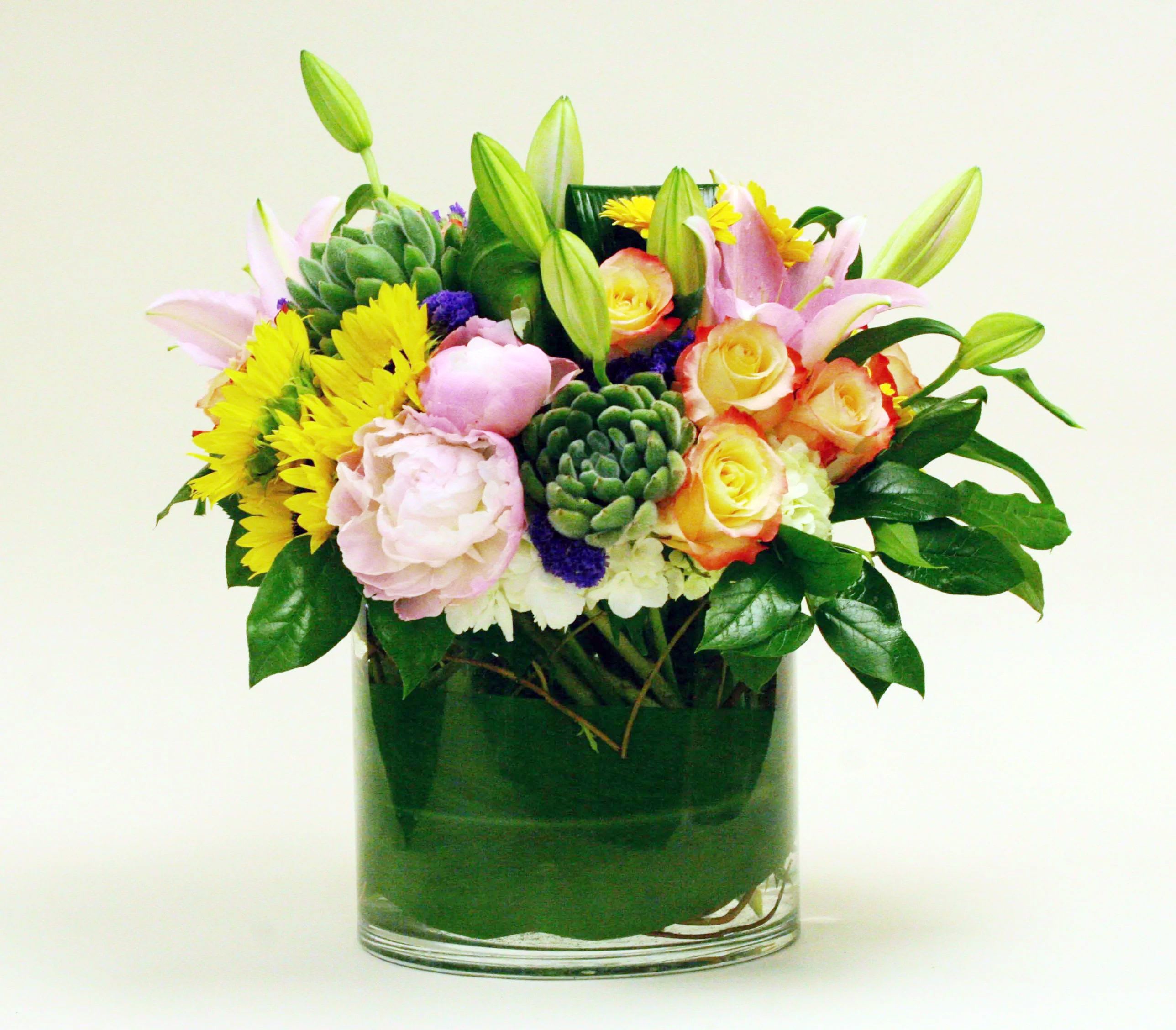 Mixed bouquet of pink lilies, yellow daisies, and roses in a glass vase