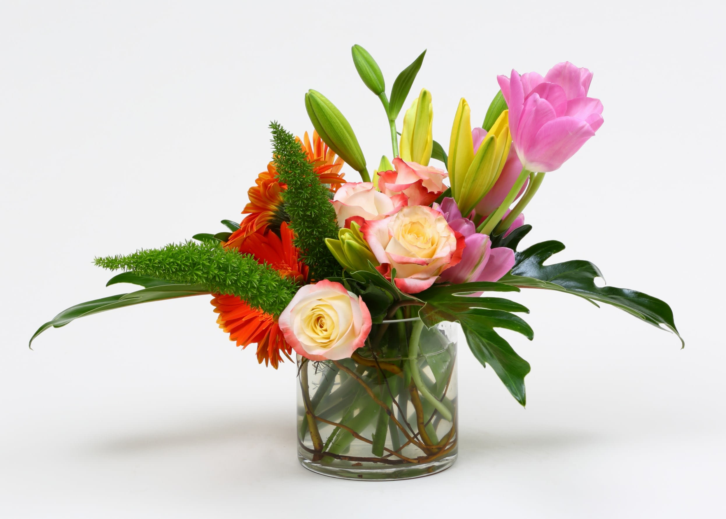 Mixed bouquet of pink tulips, roses, and orange flowers in a glass vase