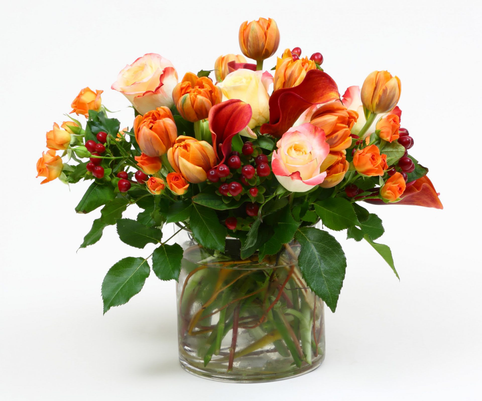 Orange and cream tulips with red berries in a glass vase
