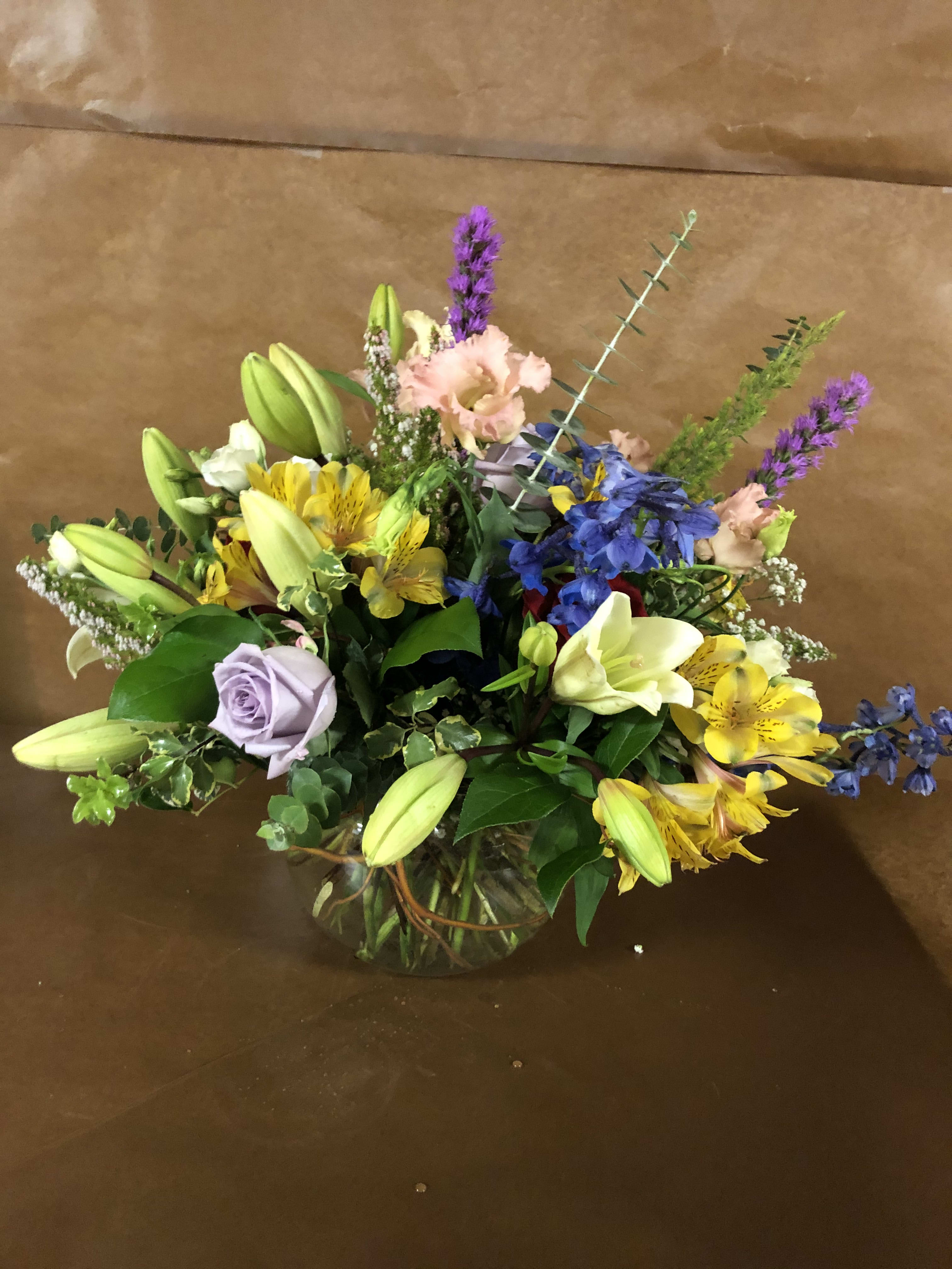 Mixed bouquet in a glass vase with lilies, roses, and blue flowers