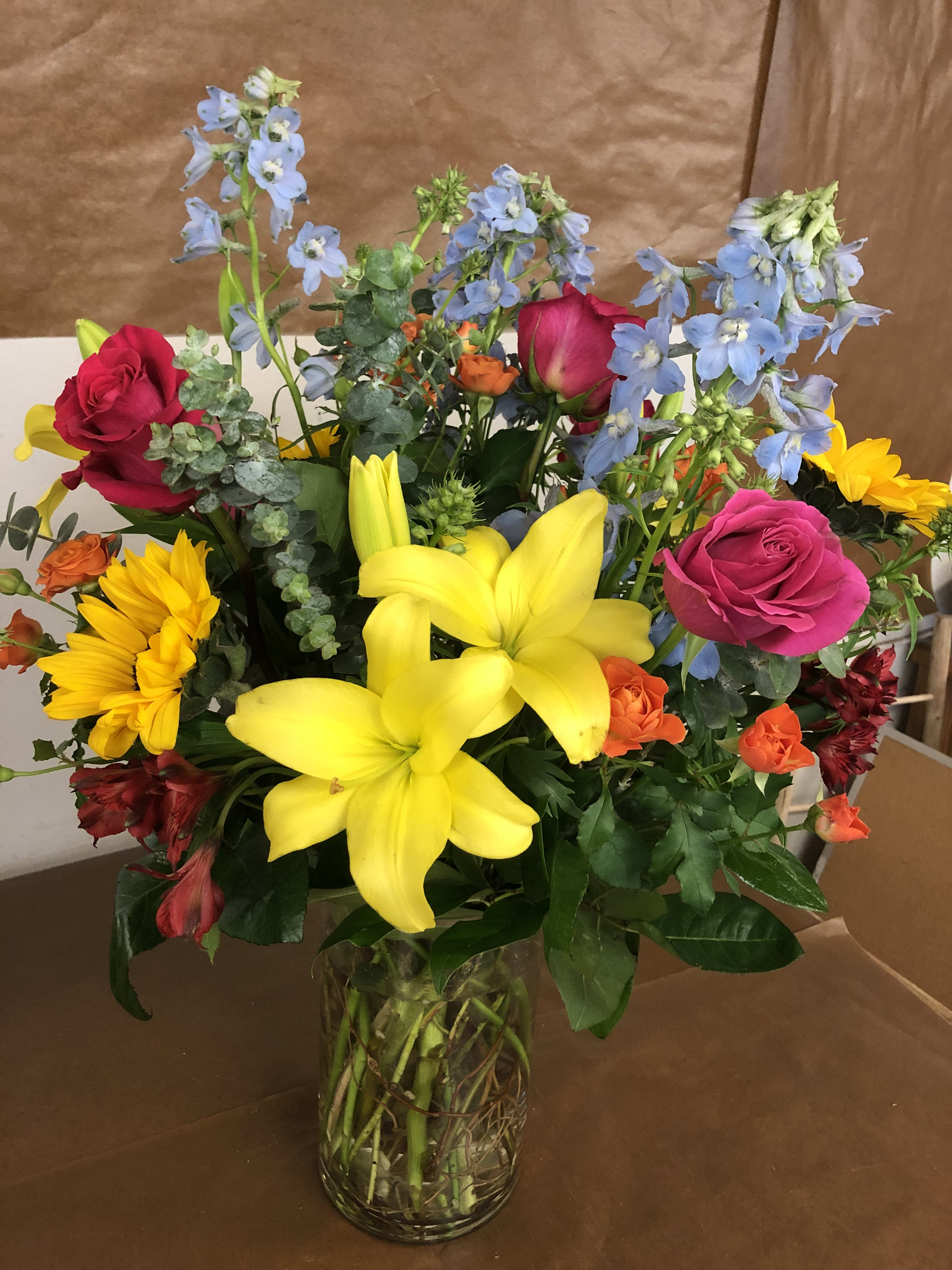 Mixed bouquet of lilies, roses, and blue delphinium in a glass vase
