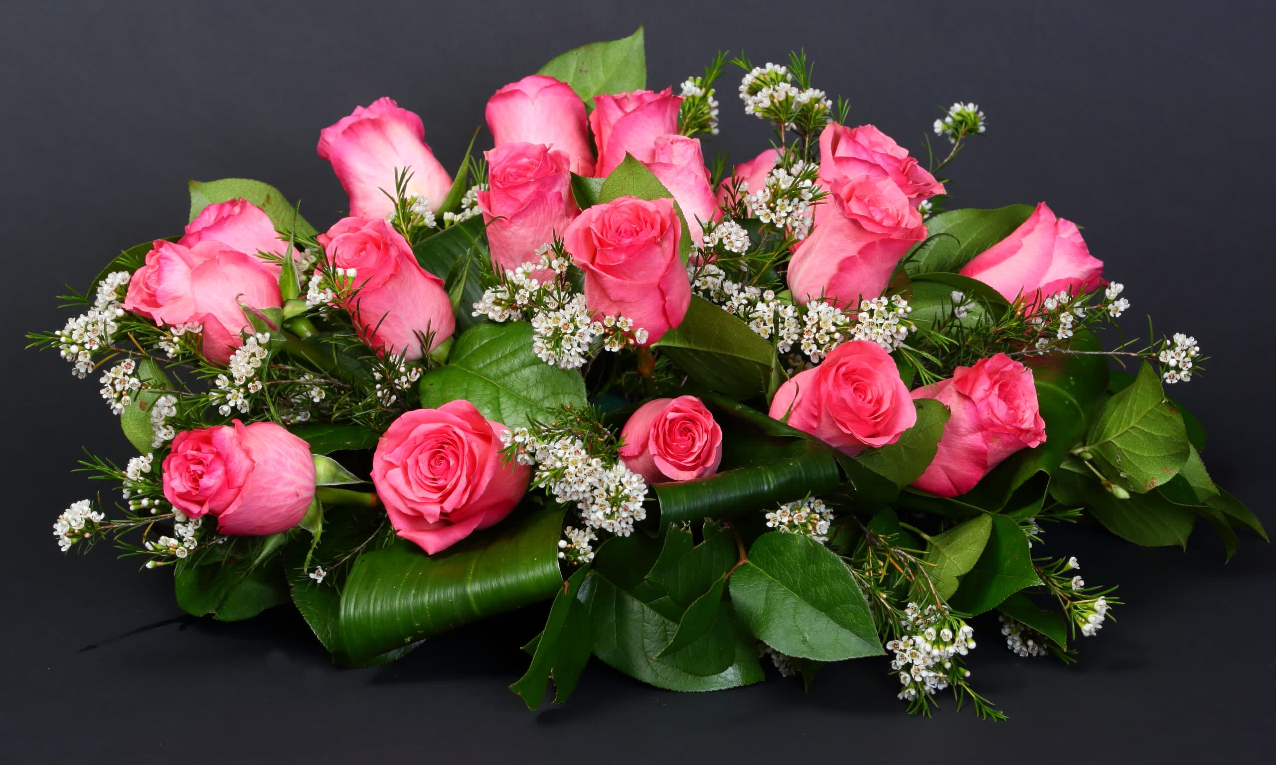 Pink roses arranged with small white filler flowers and greenery