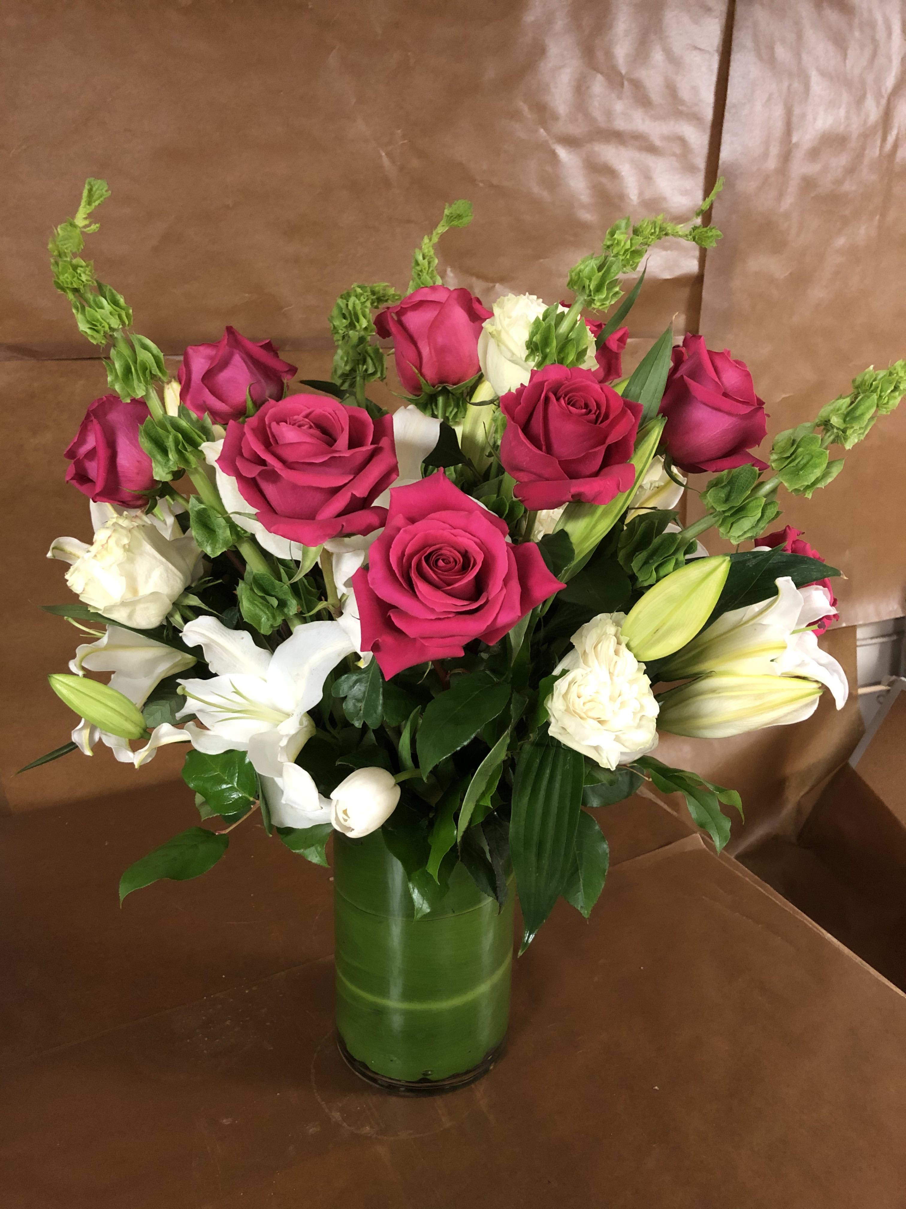 Pink and white roses with lilies in a green glass vase